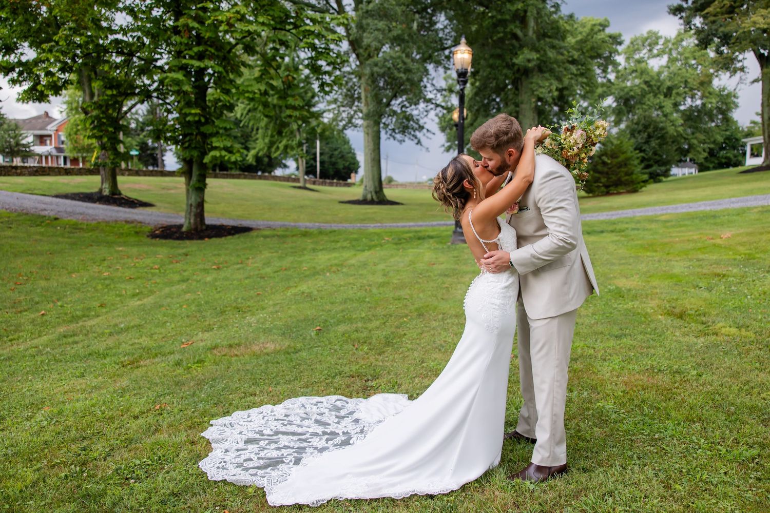 Bride and groom kissing on a green lawn with the bride’s lace train spread behind her.