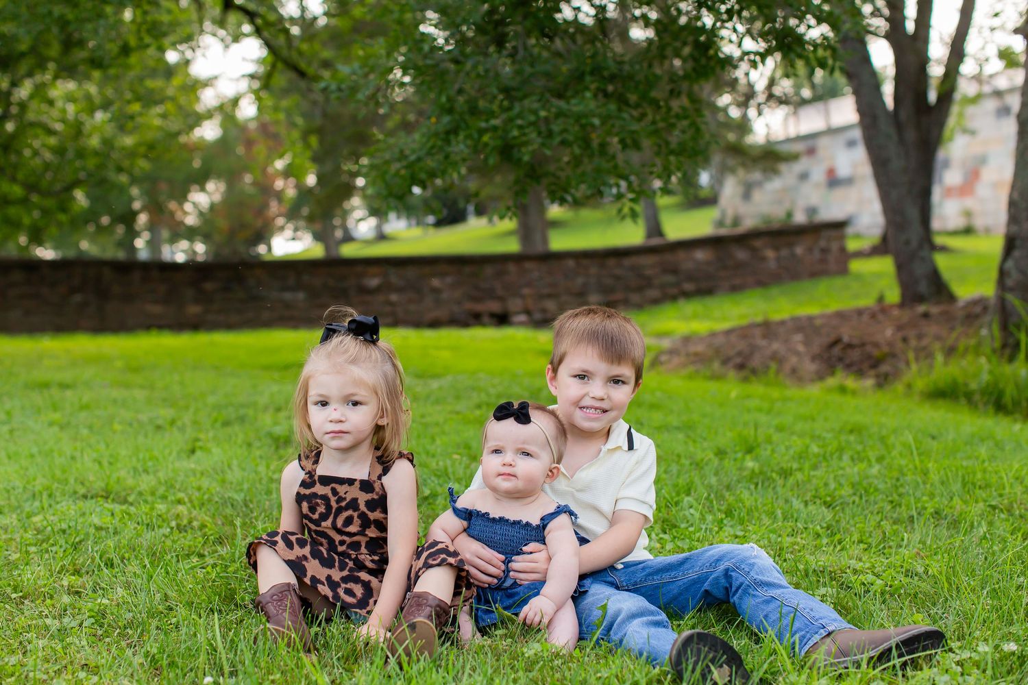 Three young children sitting close together for a family portrait outdoors.