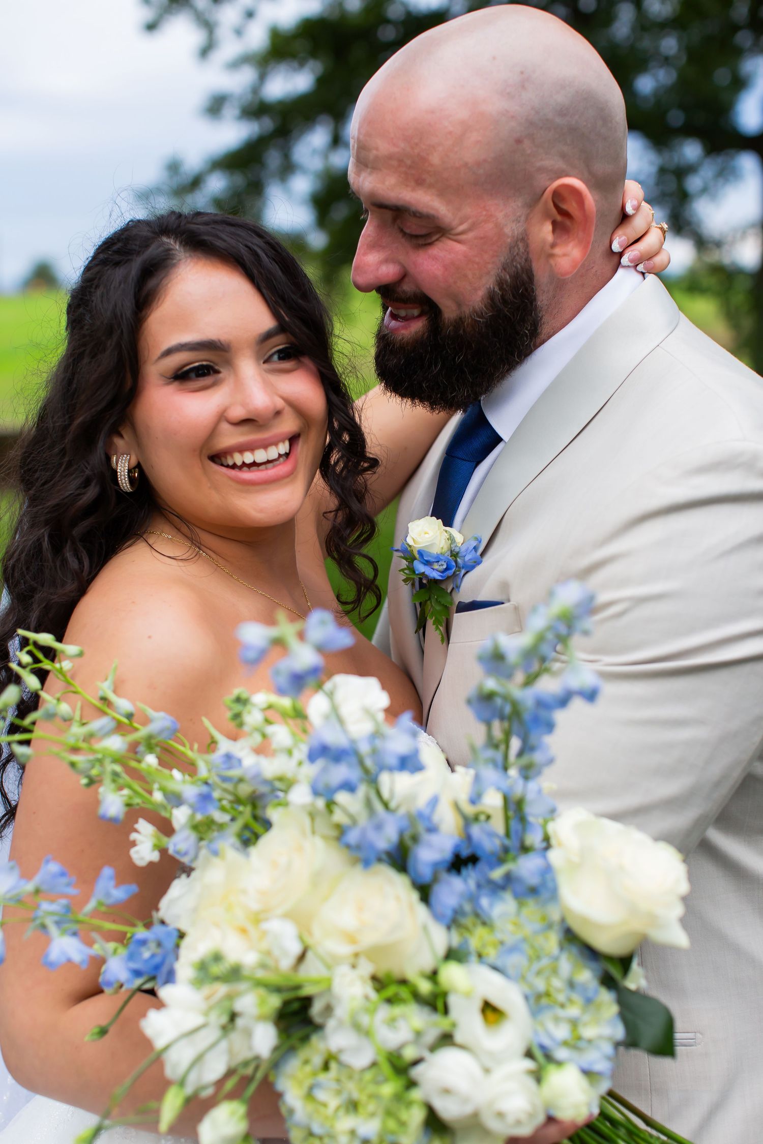 Smiling bride holding a blue and white bouquet beside her groom.