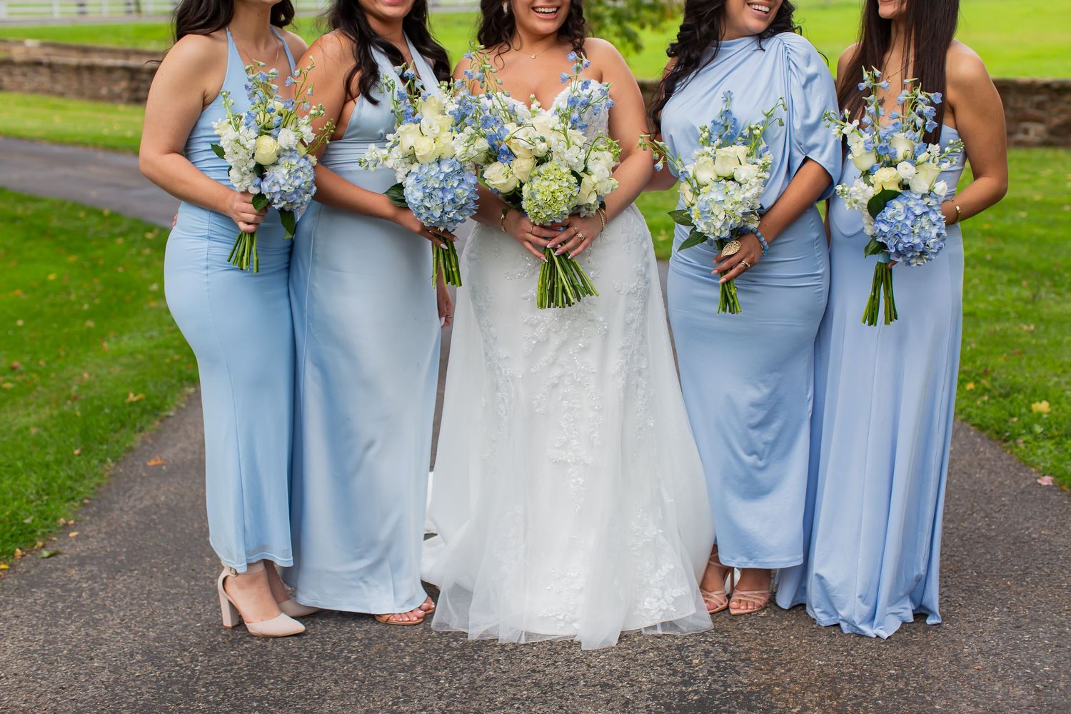 Bride and bridesmaids in pale blue dresses holding bouquets outdoors.