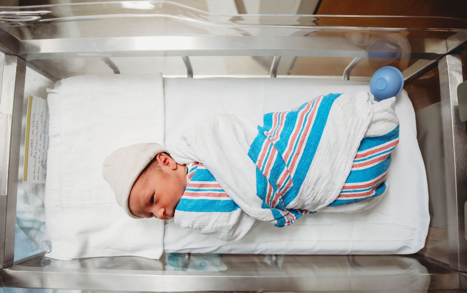 Newborn wrapped in a striped hospital blanket resting in a bassinet.