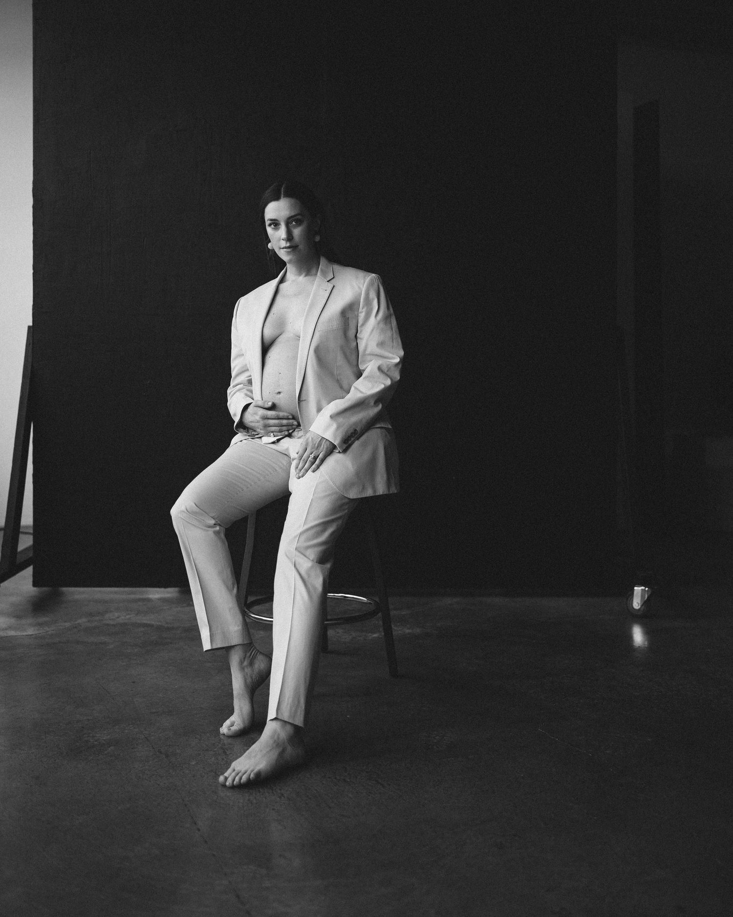 Black and white portrait in a minimal studio setting showing a person in an all-white suit and bare feet.