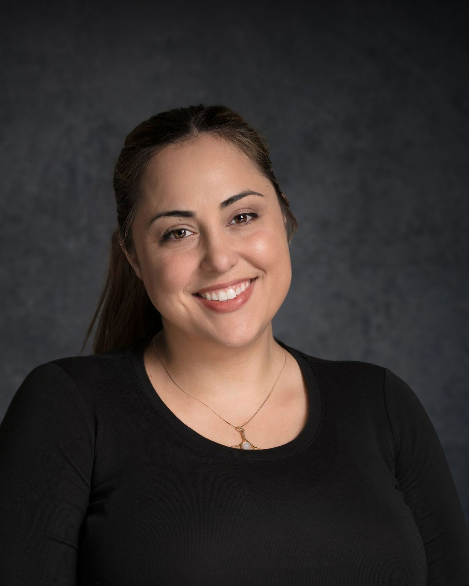 Professional studio portrait with warm smile against dark gray background.