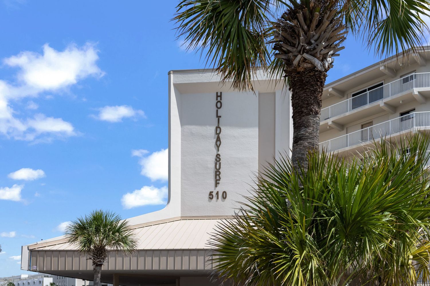 Beachfront condo building with palm trees and blue sky, professional real estate photo by Coast Captured Emerald Coast