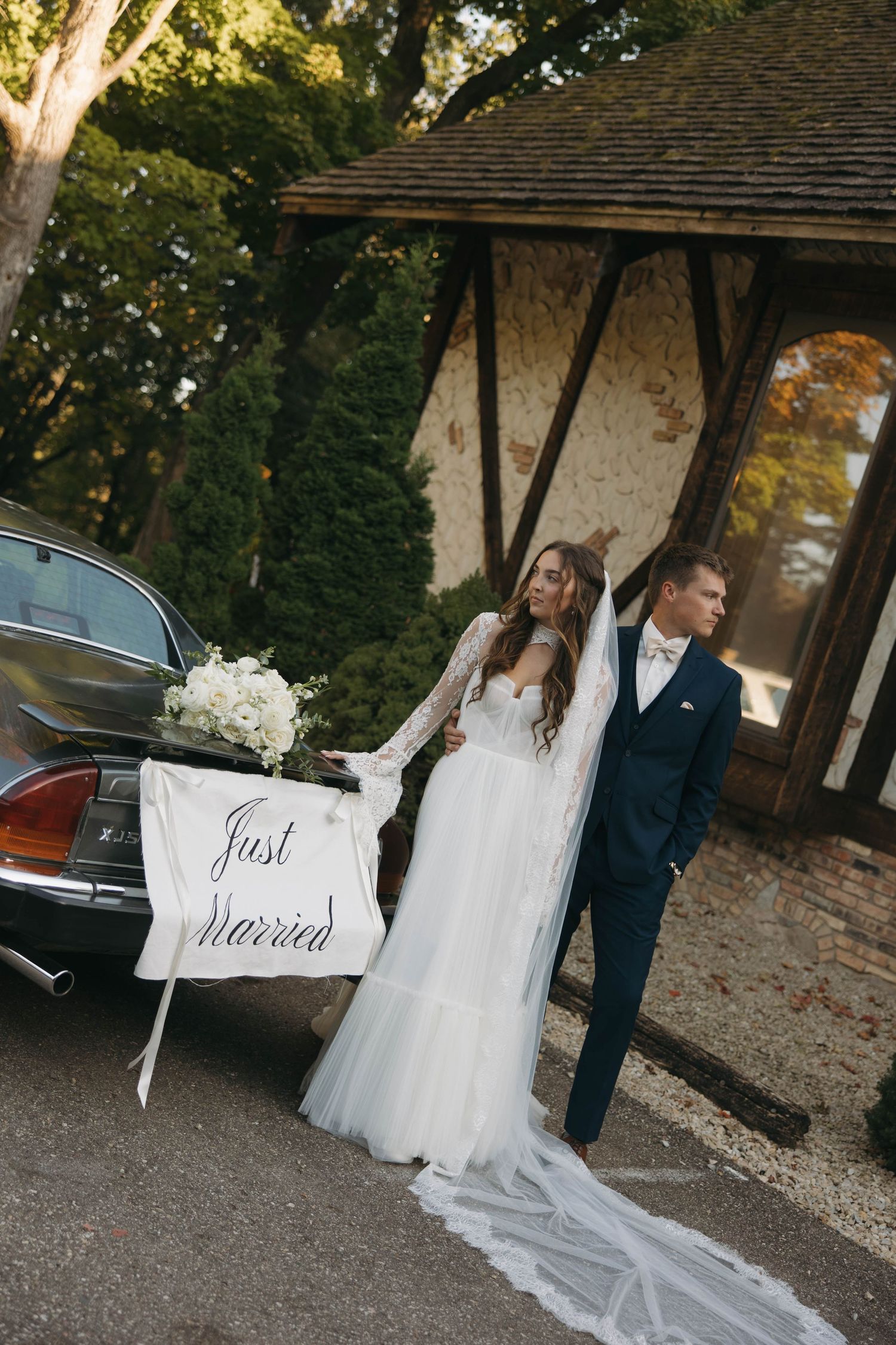 Newlywed couple holding 'Just Married' signs while standing together outside a rustic building.