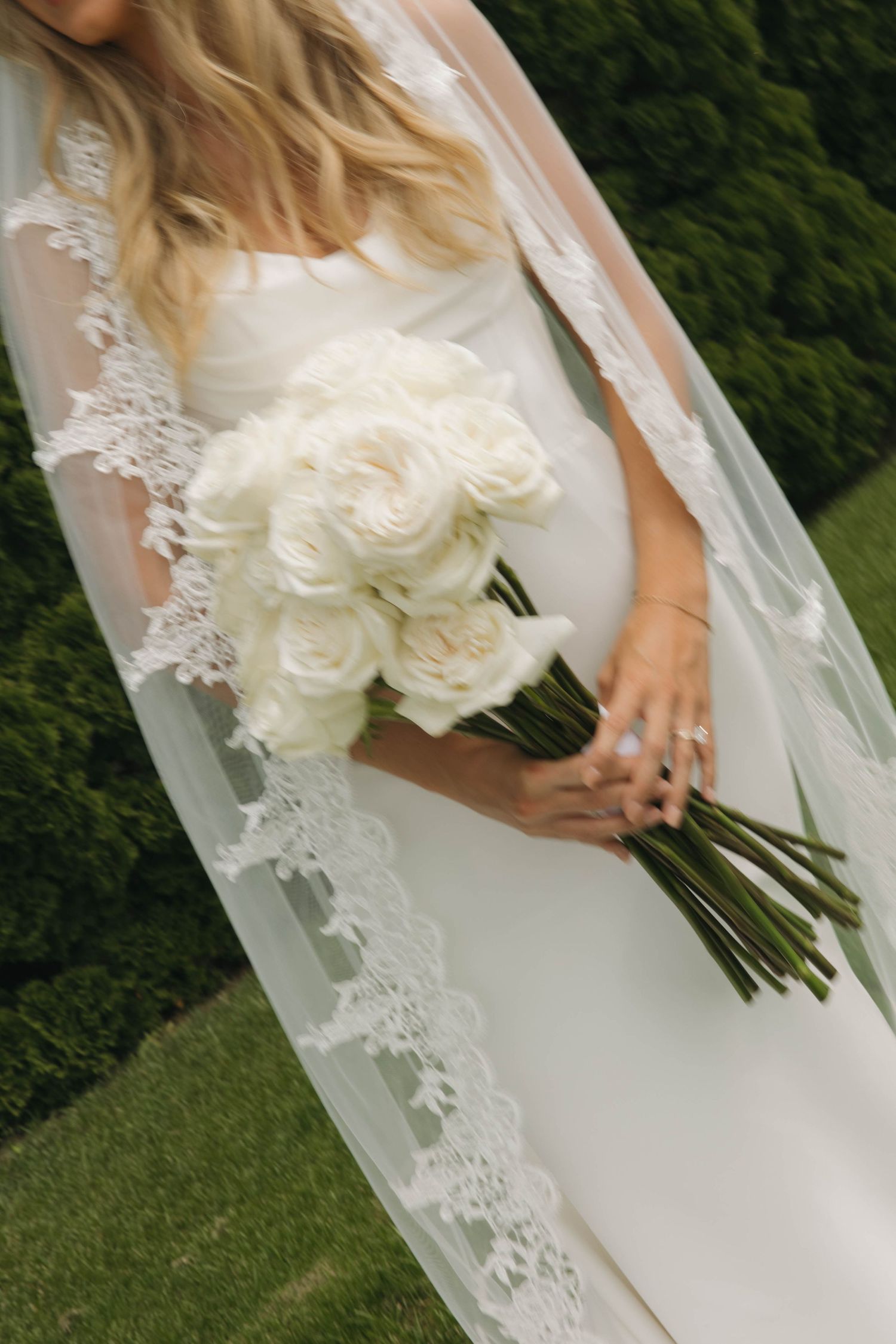 Close-up view of white roses in a bridal bouquet with lace veil details against a green outdoor background.