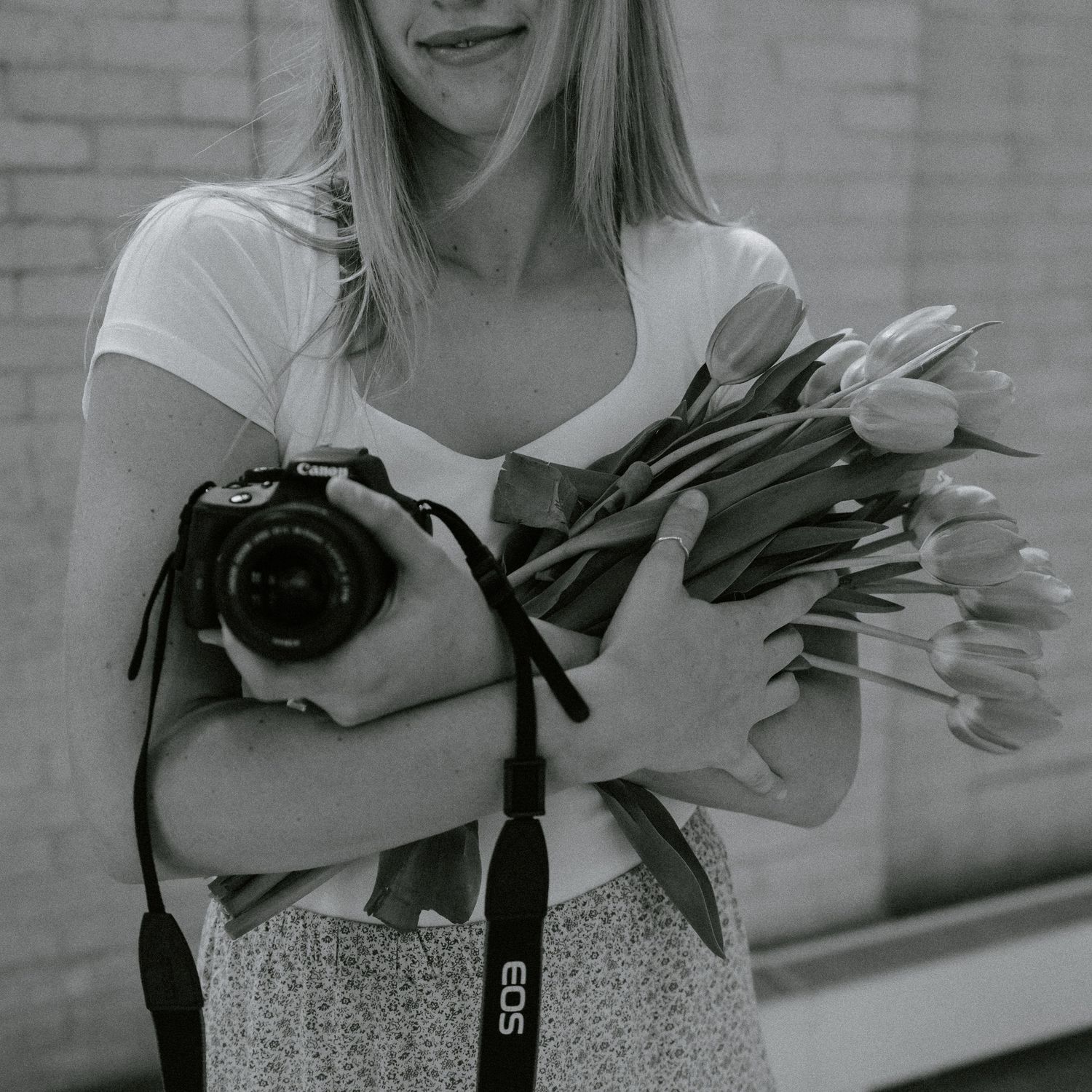 Black and white luxury photo of photographer artfully holding a camera and tulips.