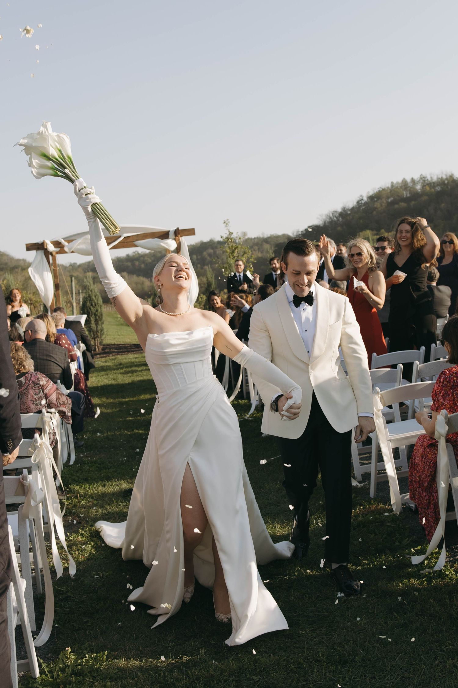 Joyful wedding couple dances together outdoors during sunset celebration with guests in white chairs.
