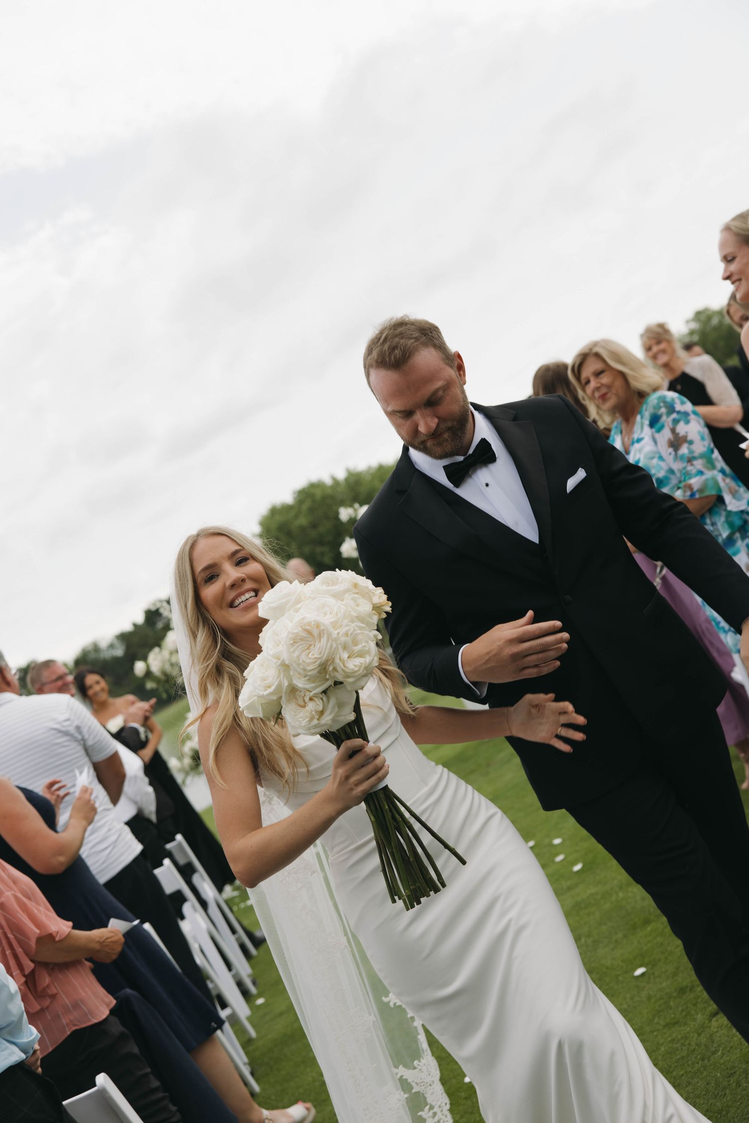 Wedding celebration on a grassy lawn with guests in formal attire enjoying a joyful moment.