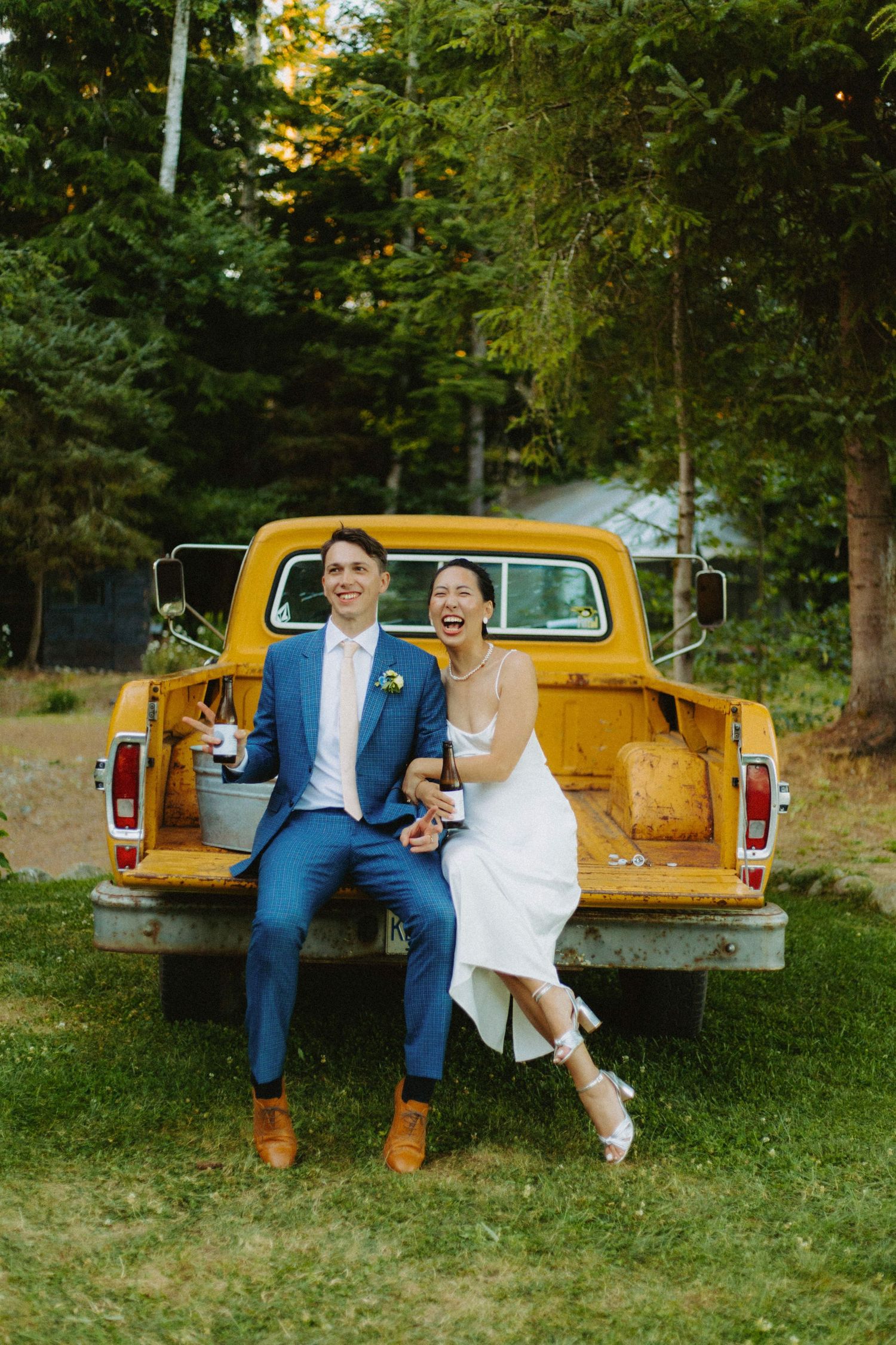 Couple sits together on vintage yellow pickup truck during outdoor wedding photoshoot.