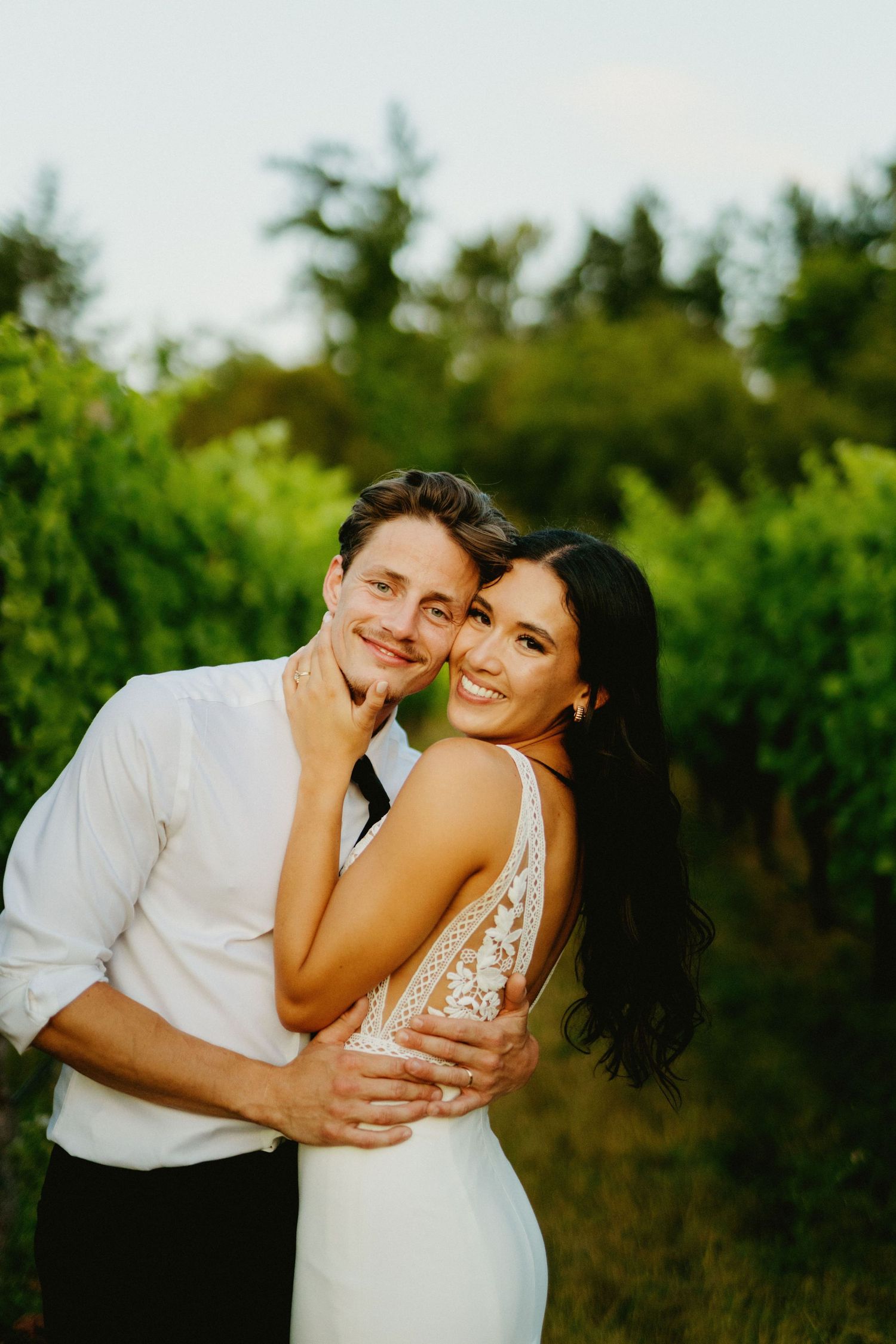 A couple shares joyful moments outdoors against a backdrop of green foliage.