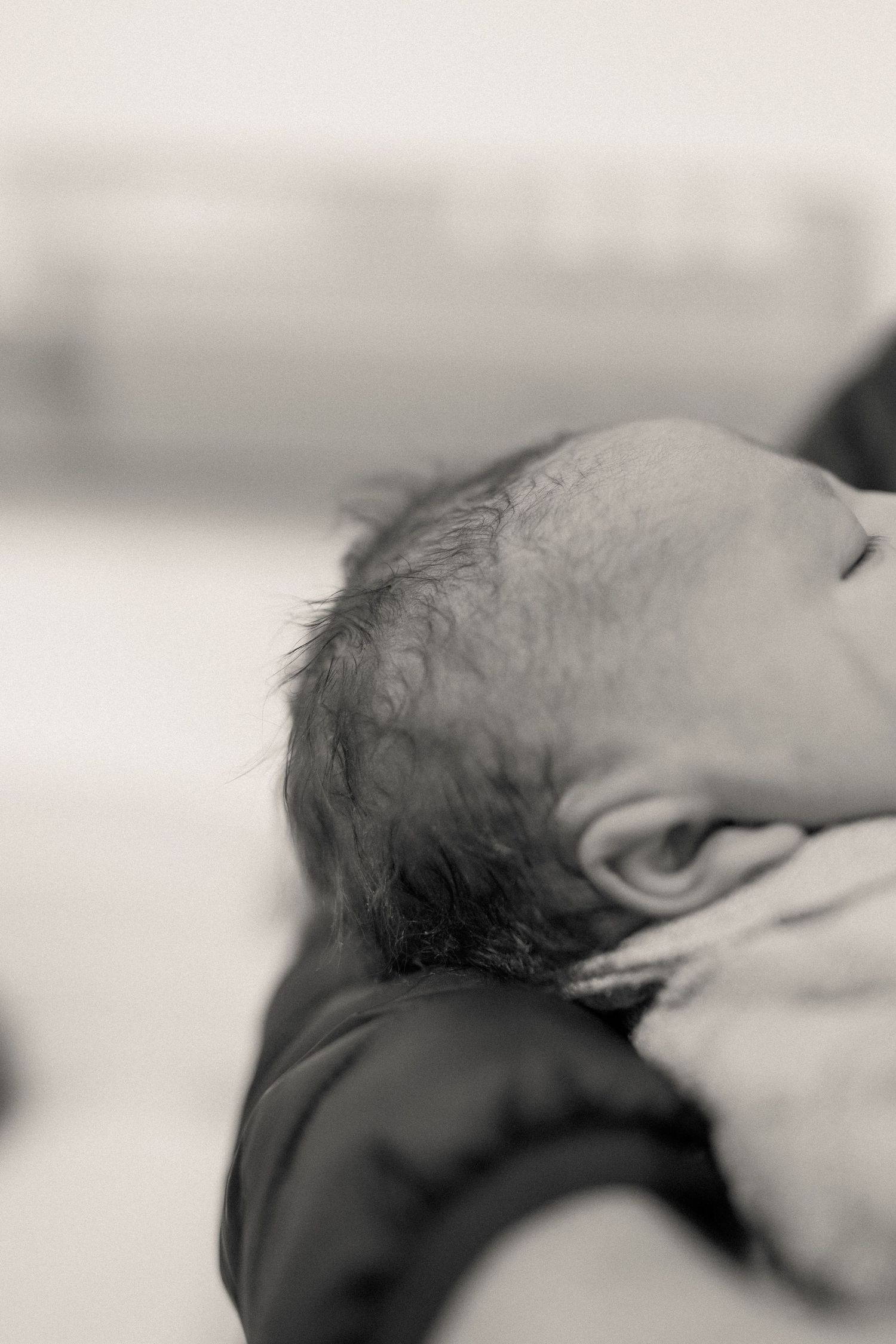 Black and white close-up photo of a sleeping newborn baby cradled in an adult's arms.
