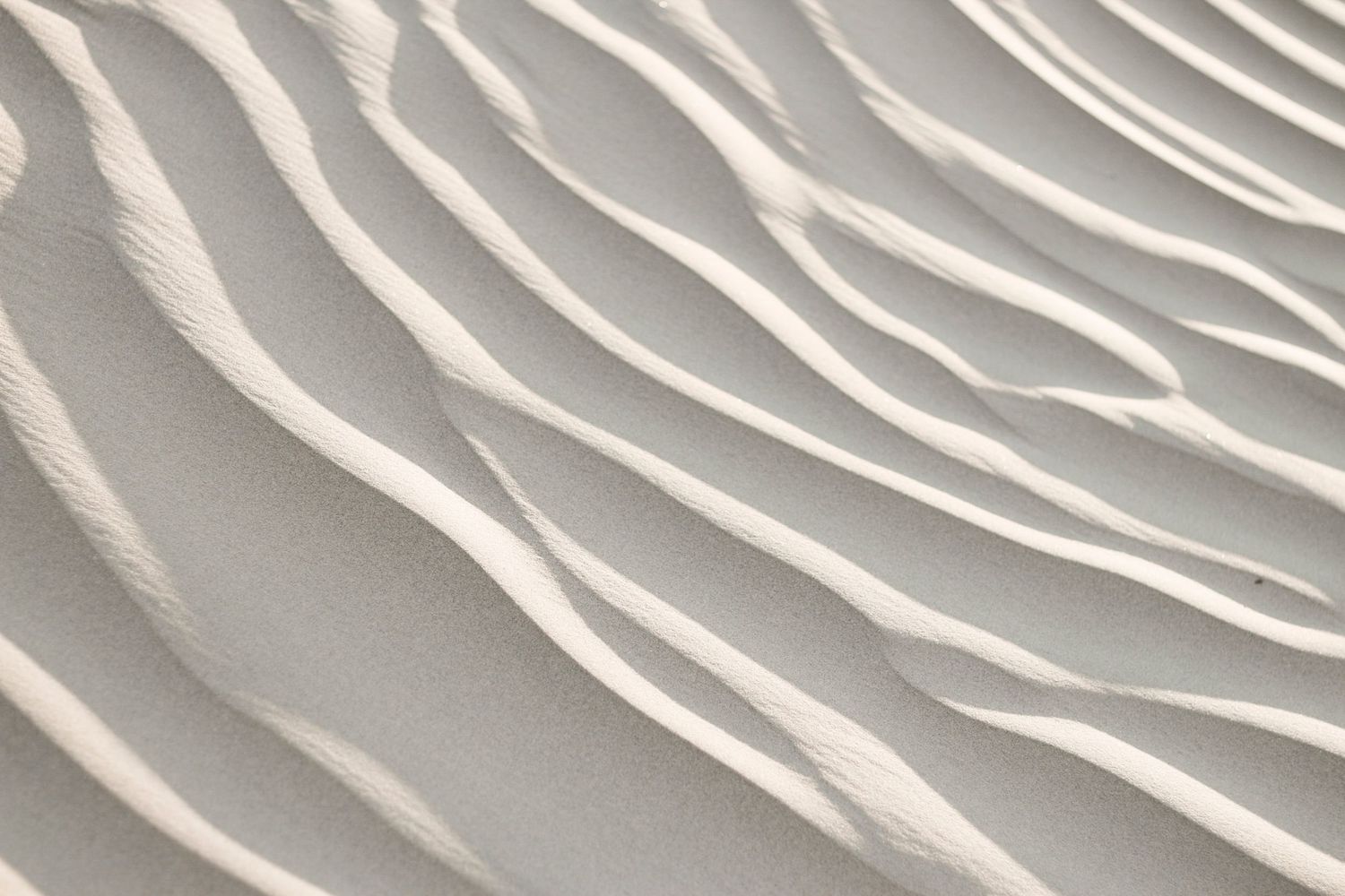 Close-up of white sand dunes with rippling wave-like patterns and ridges creating a textured natural abstract background.