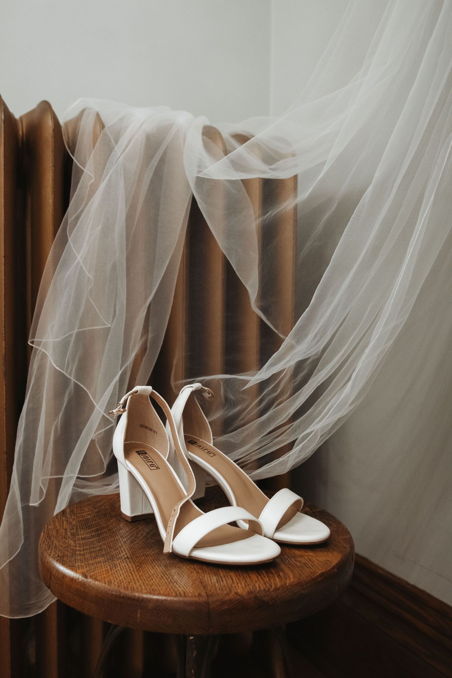 White block heel bridal sandals displayed on wooden stool with flowing veil.