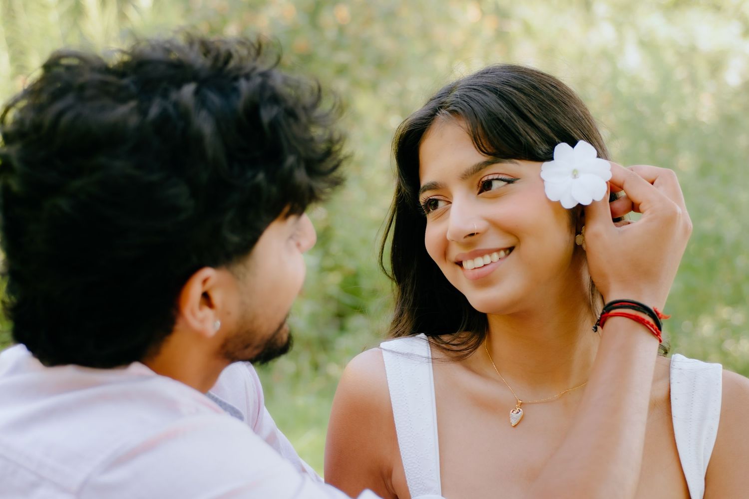 A young man placing a white flower in a smiling woman's hair outdoors.