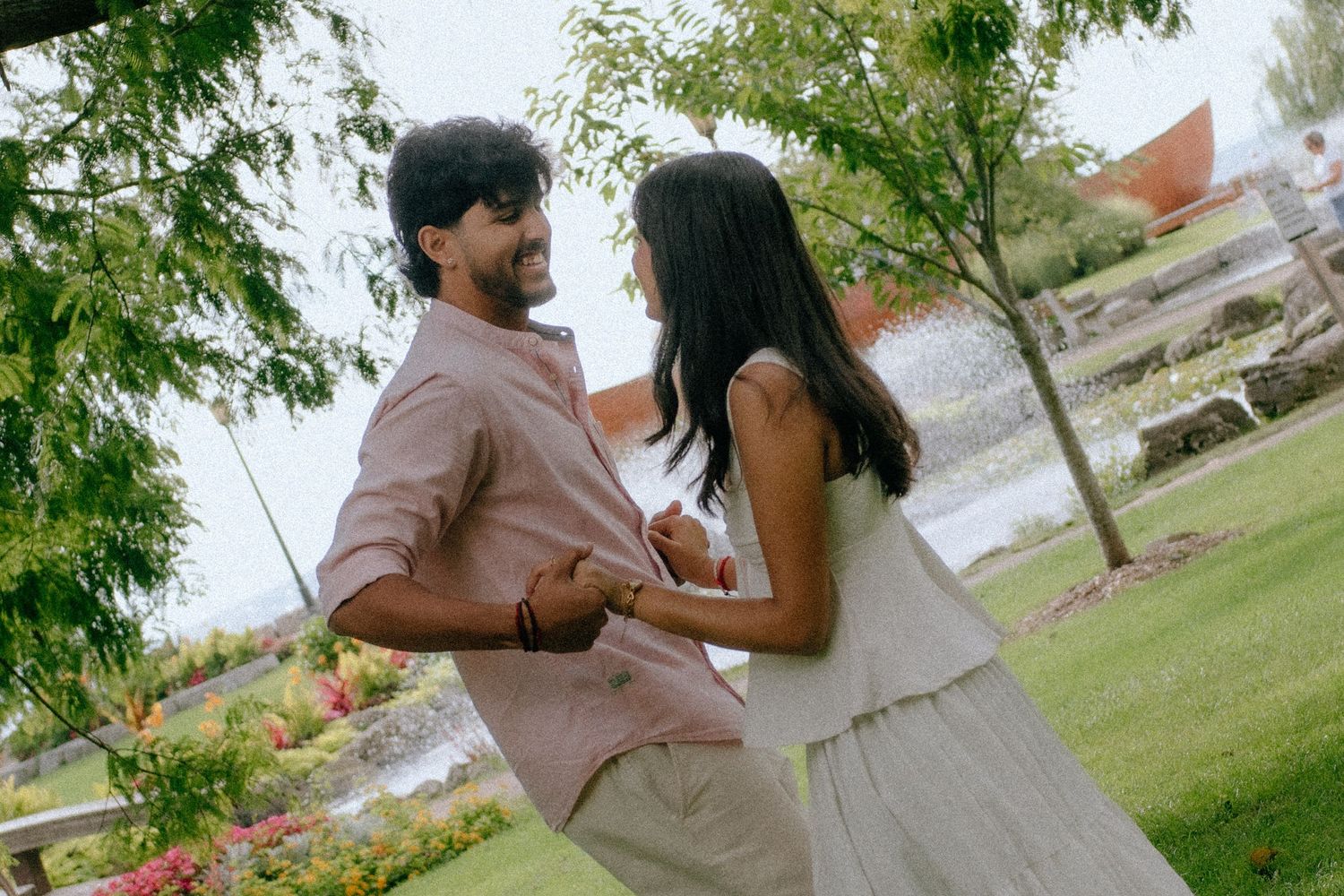 A couple dancing and holding hands in a lush green park near a pond.