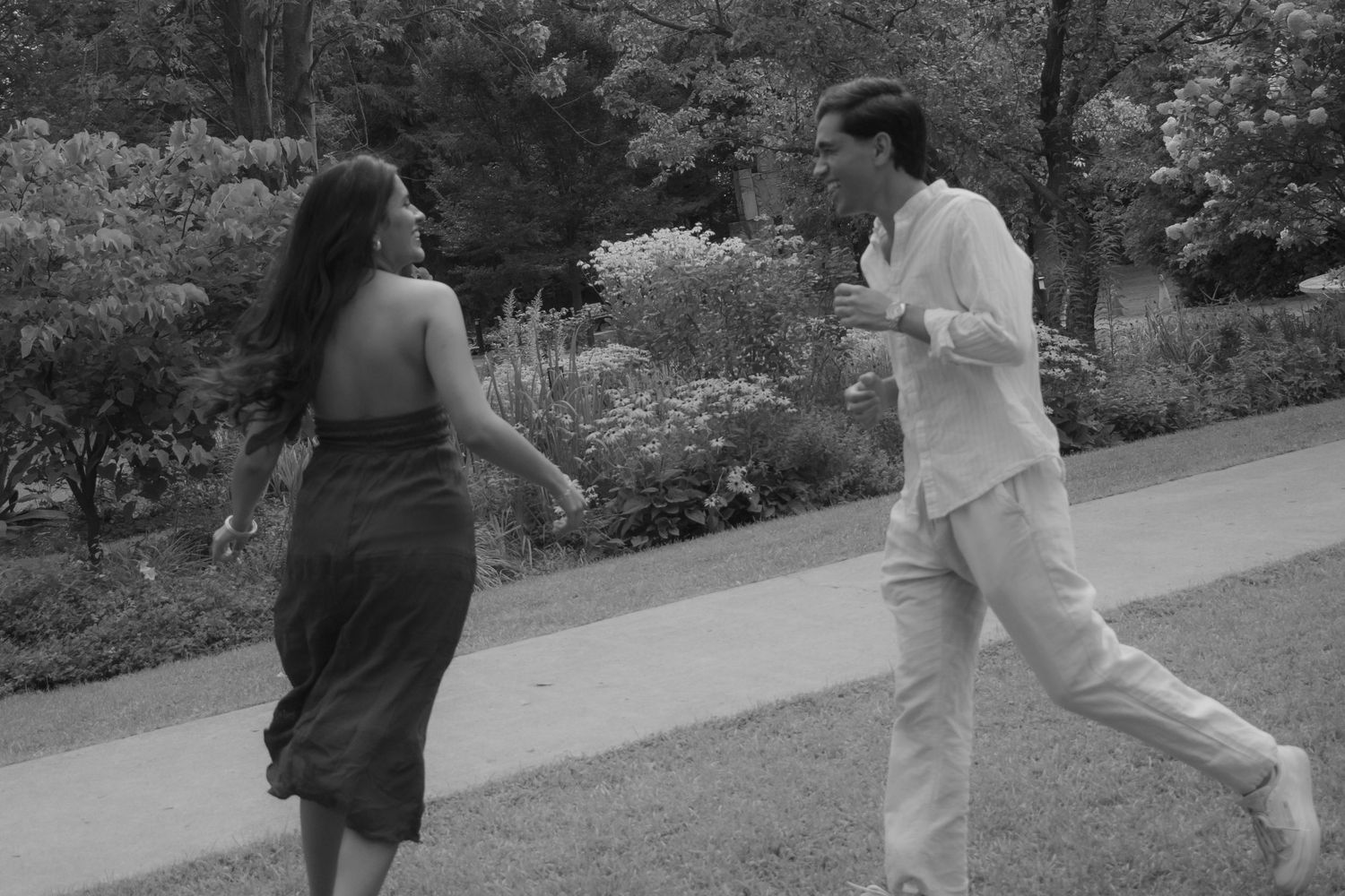Black and white photo of a couple dancing together on a garden path surrounded by lush greenery.