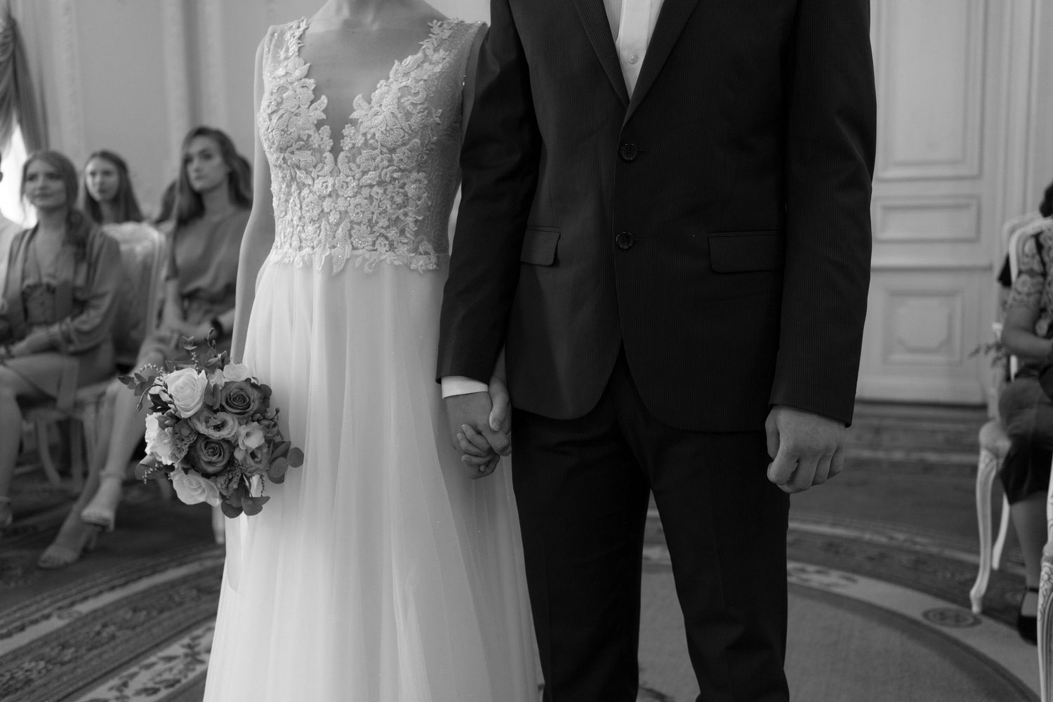 Black and white photo of bride and groom holding hands during wedding ceremony.