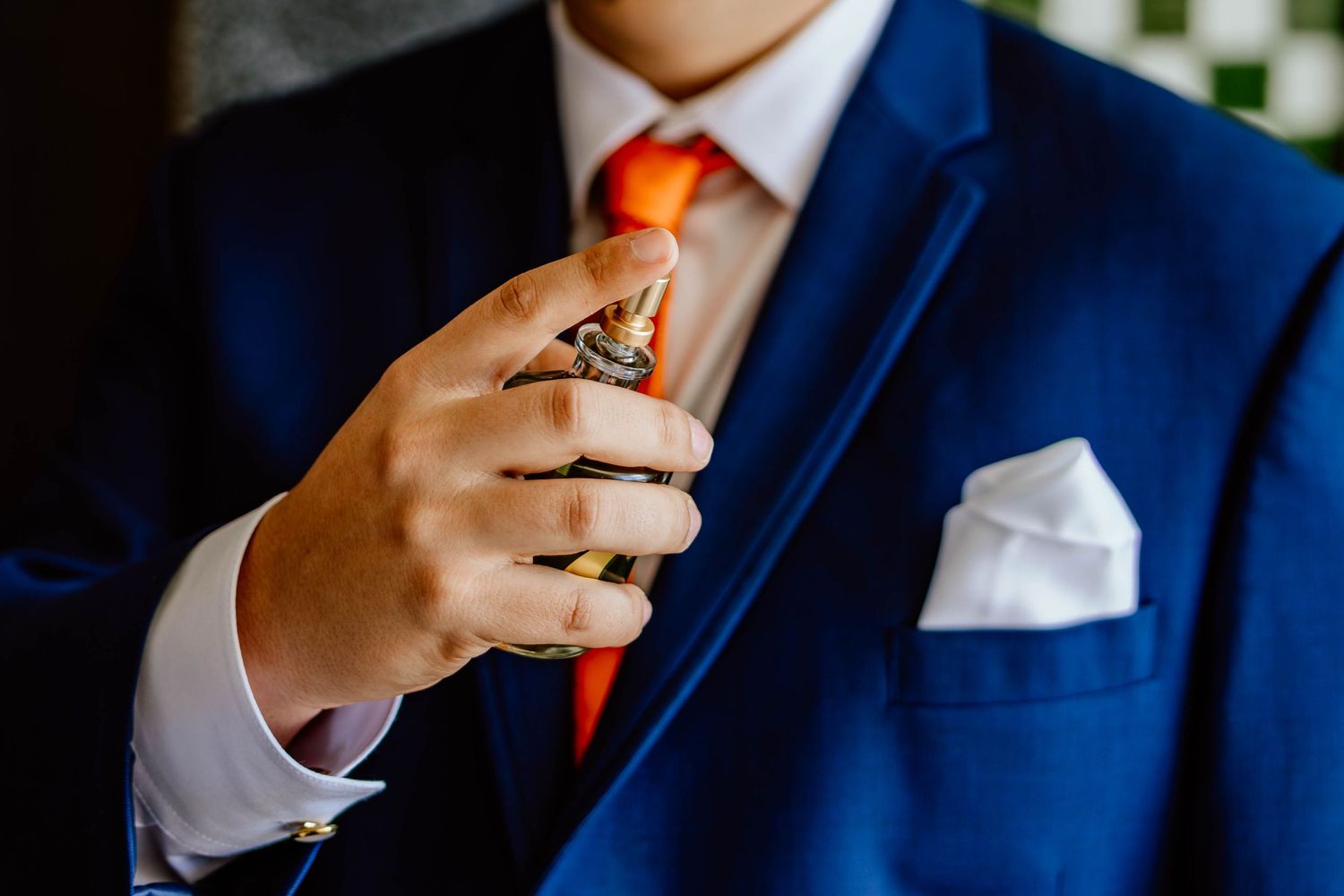 Groom in blue suit with orange tie applying cologne before the wedding ceremony. Chicago hotel wedding photos.