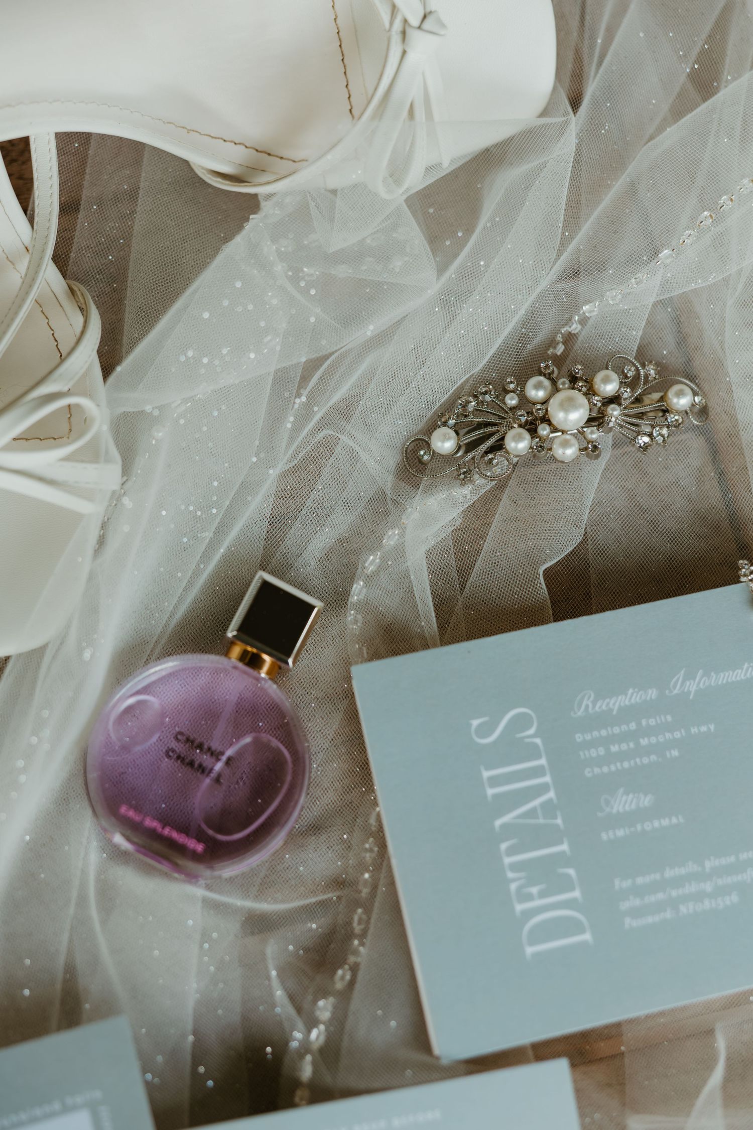 Bridal flat lay featuring Chanel perfume, pearl hair clip, and sage green wedding invitation details. Northwest Indiana wedding venues.