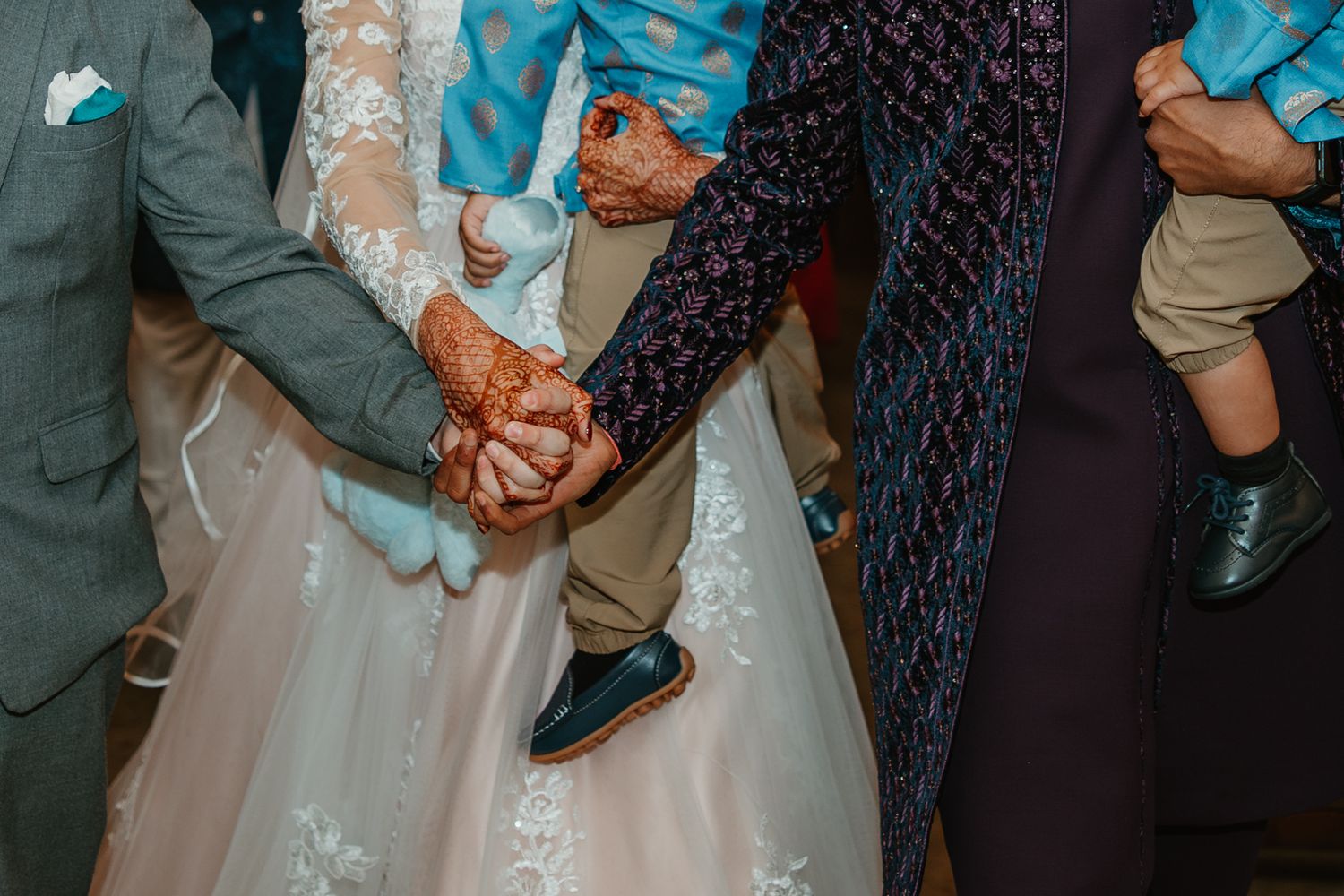 Bride with henna hands holds groom and family member hands during wedding ceremony. Documentary style wedding photos.