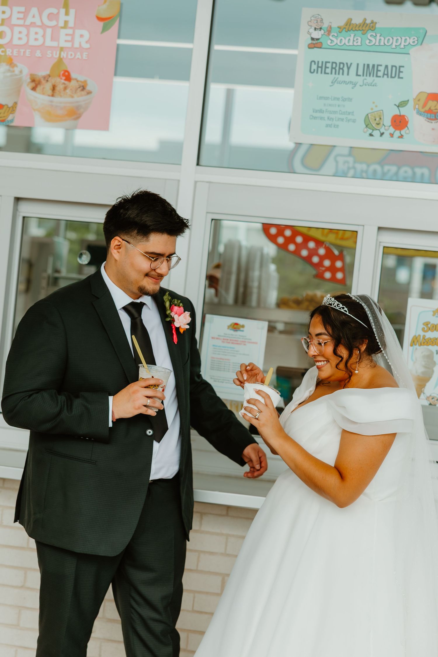 Bride in white off-shoulder gown and groom in black suit enjoying ice cream outside Sonic on wedding day. Chicagoland wedding venues.