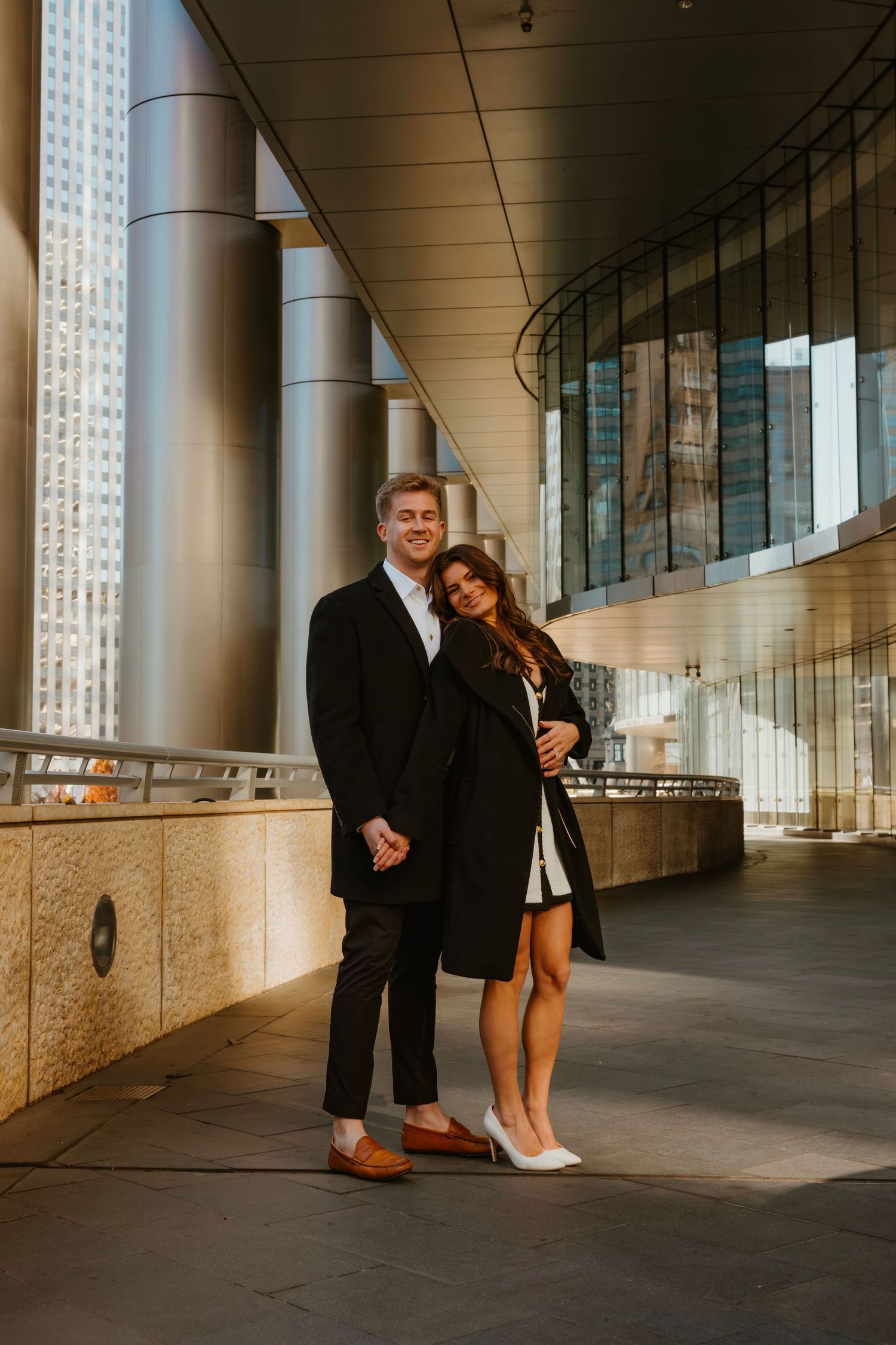 Couple posing together in black outfits at modern Chicago architecture with golden light. Outdoor Chicago engagement photos.
