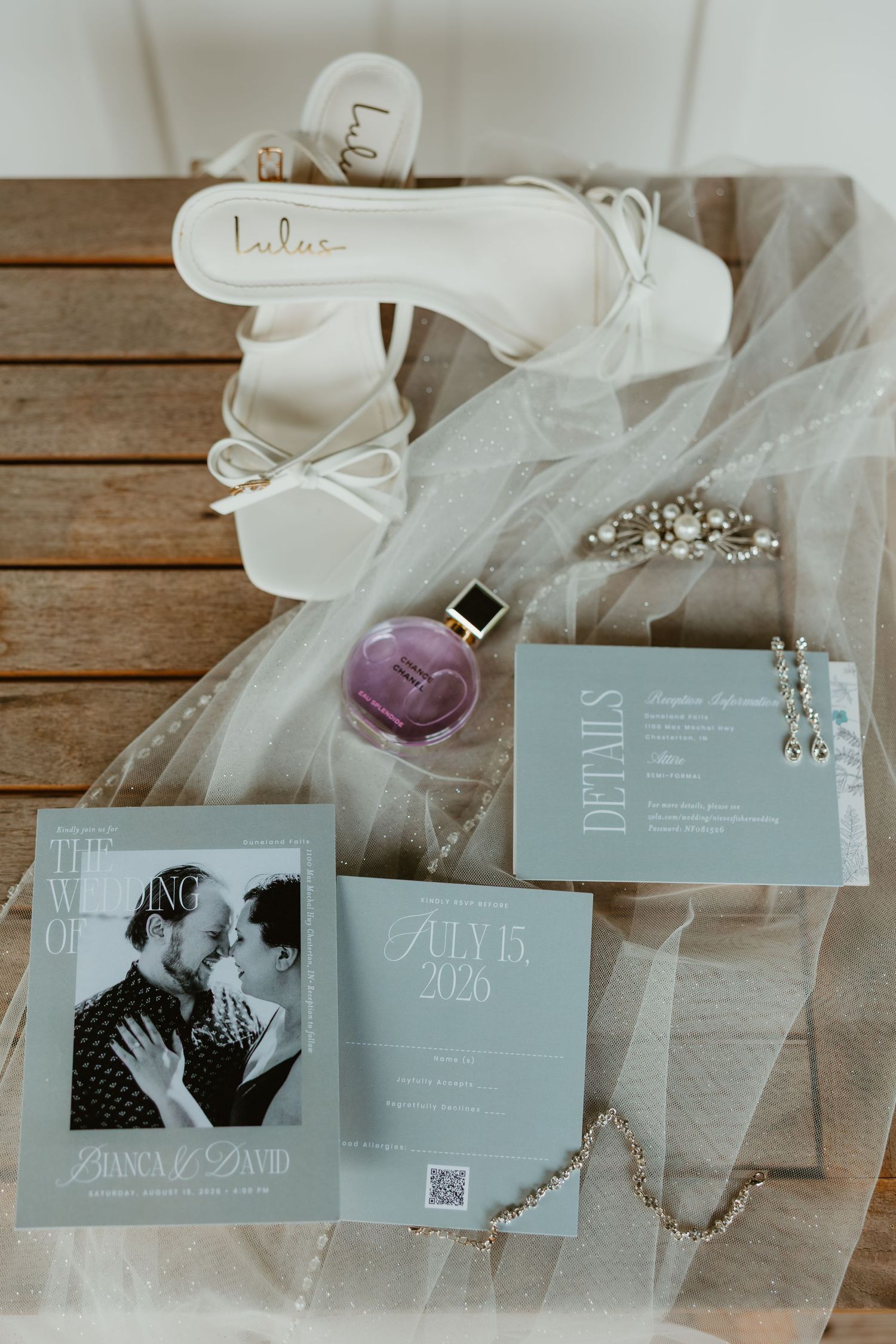 Wedding flat lay with white Lulus heels, sage invitations, perfume, and veil for July 15 2026 wedding. Northwest Indiana wedding venues.