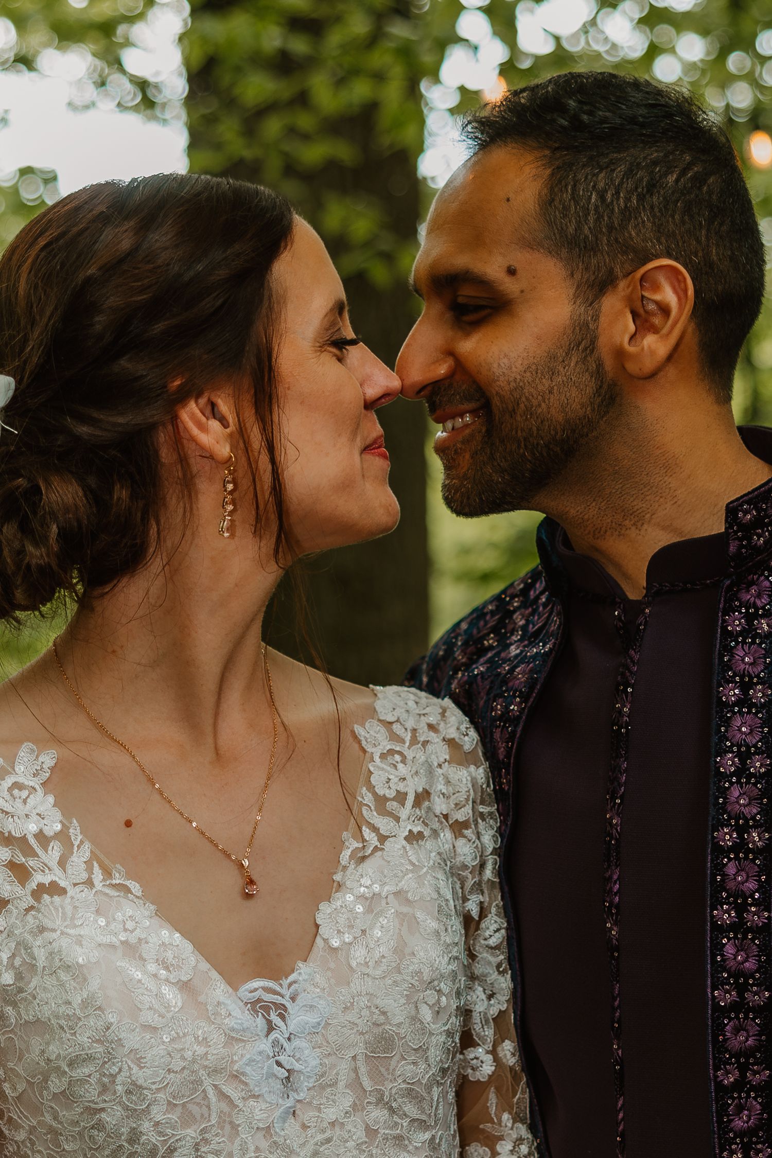 Close-up of bride and groom nose-to-nose smiling warmly in a romantic outdoor forest setting. Documentary style wedding photos.