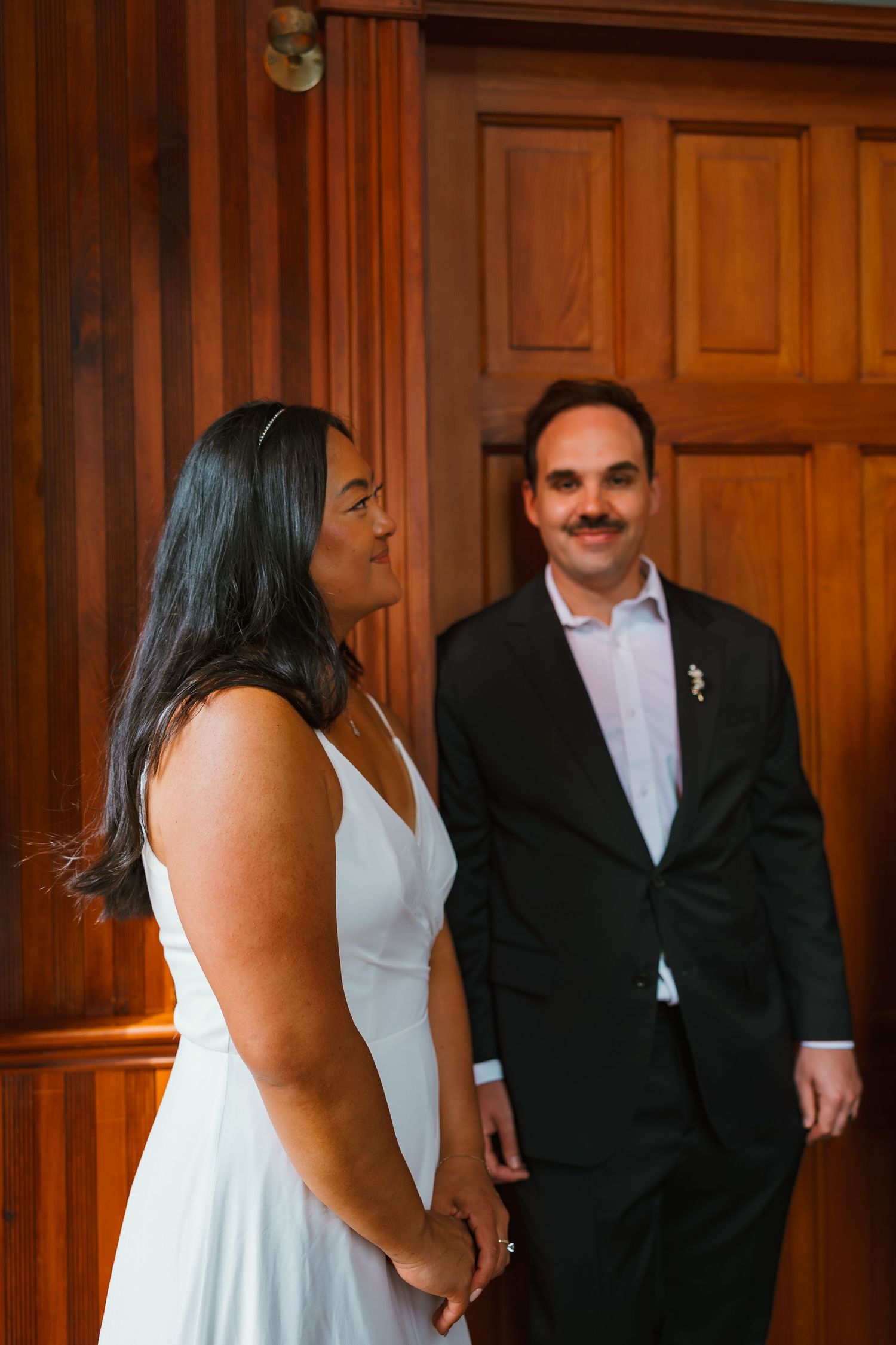 Bride and groom share a candid moment by warm wooden doors during wedding day preparations. Michigan elopement.