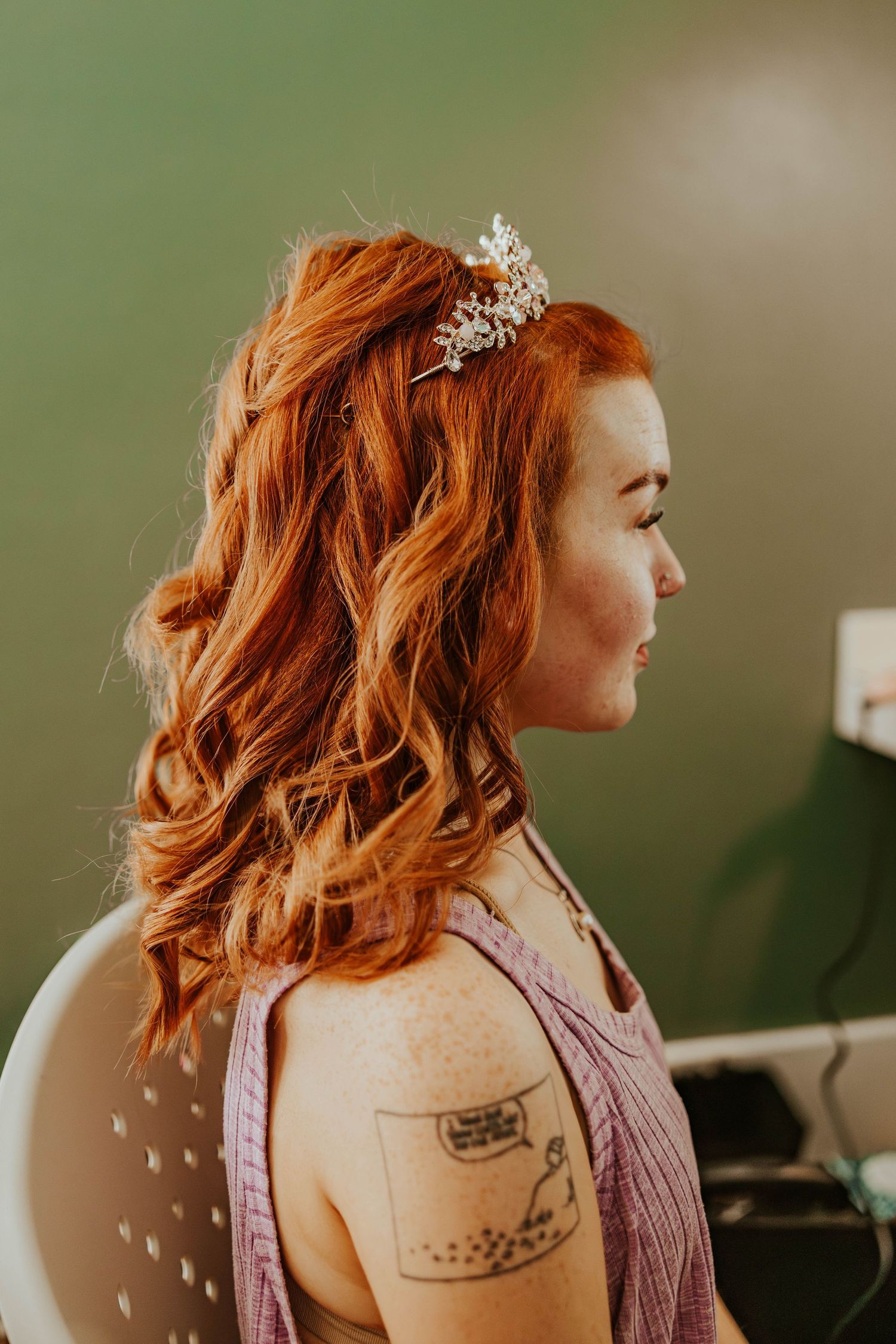 Red-haired bridesmaid in profile view wearing crystal hair comb accessory during wedding preparations.