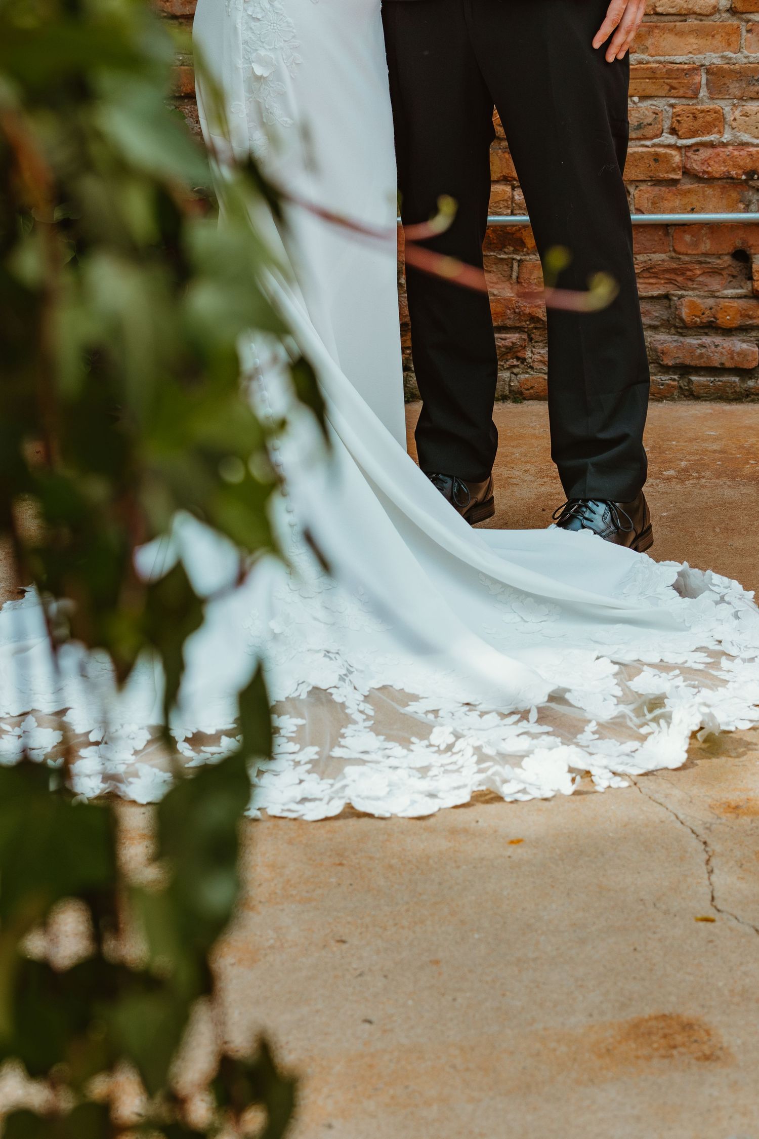 Close-up of bride's elegant lace wedding dress train on stone path near brick wall. Chicagoland wedding venues.