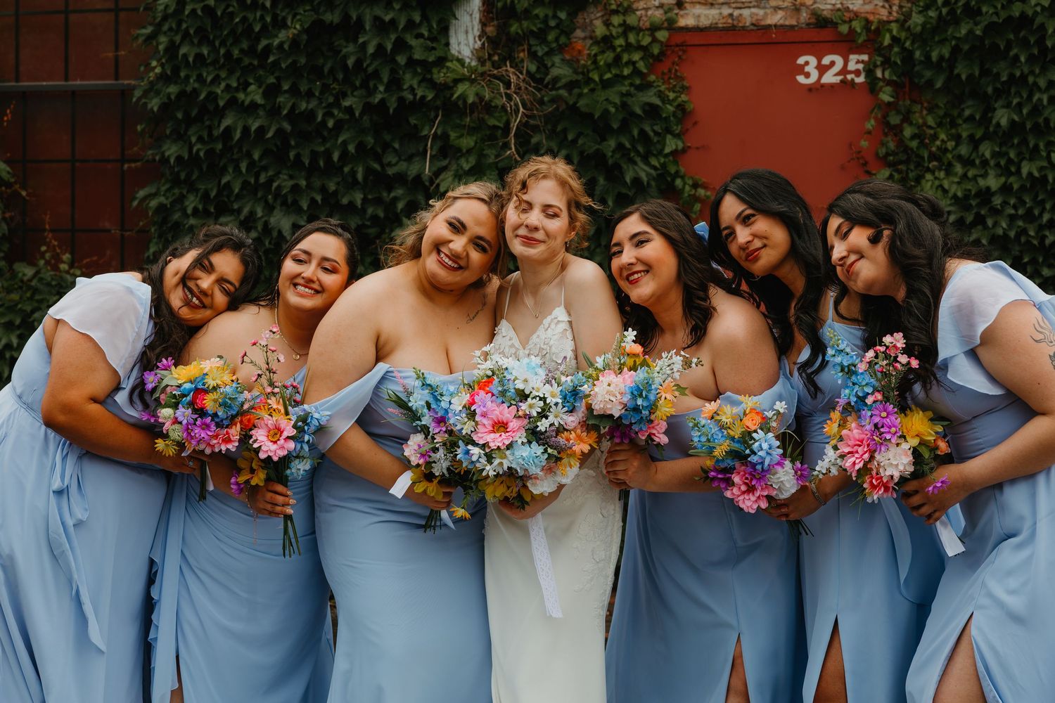 Bride in white gown with six bridesmaids in blue dresses holding colorful bouquets. Chicagoland wedding venues.