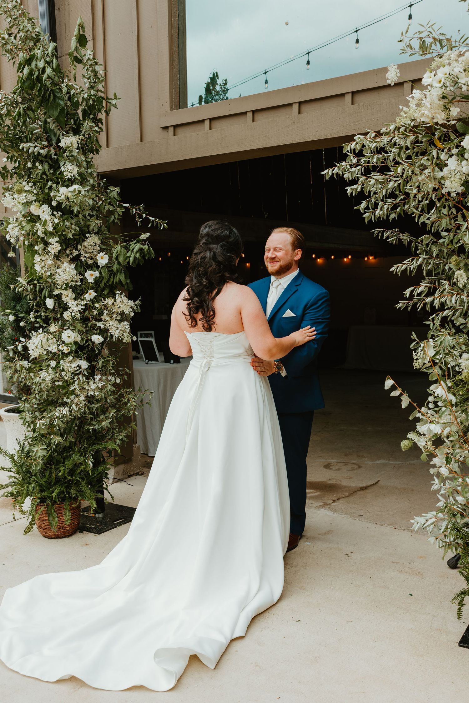 Groom smiles warmly at his bride during an emotional first look beneath a floral arch at an outdoor barn wedding. Northwest Indiana wedding