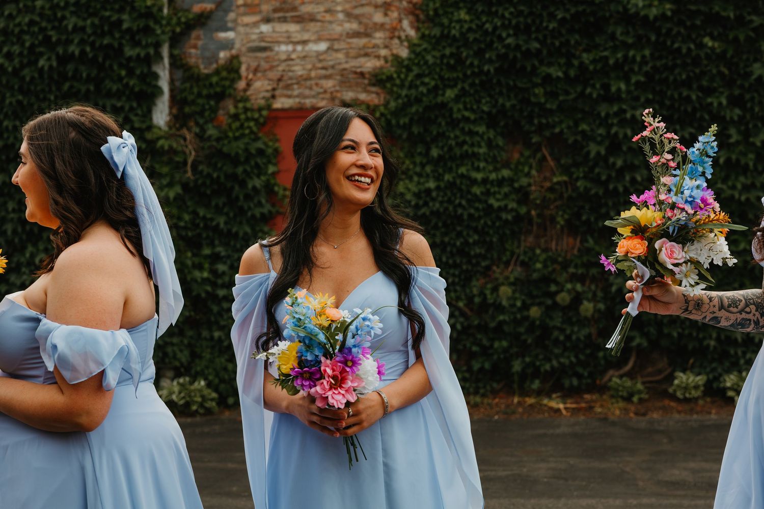 Bridesmaids in light blue dresses holding colorful bouquets laughing outdoors at wedding. Chicagoland wedding venues.