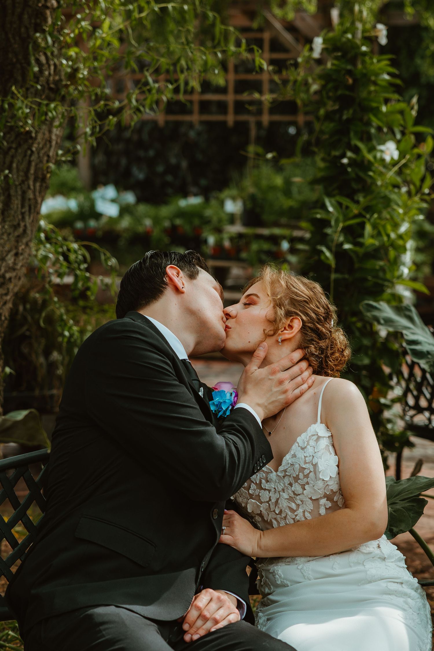 Bride and groom share romantic kiss while seated on bench in lush garden setting. Chicagoland wedding venues.