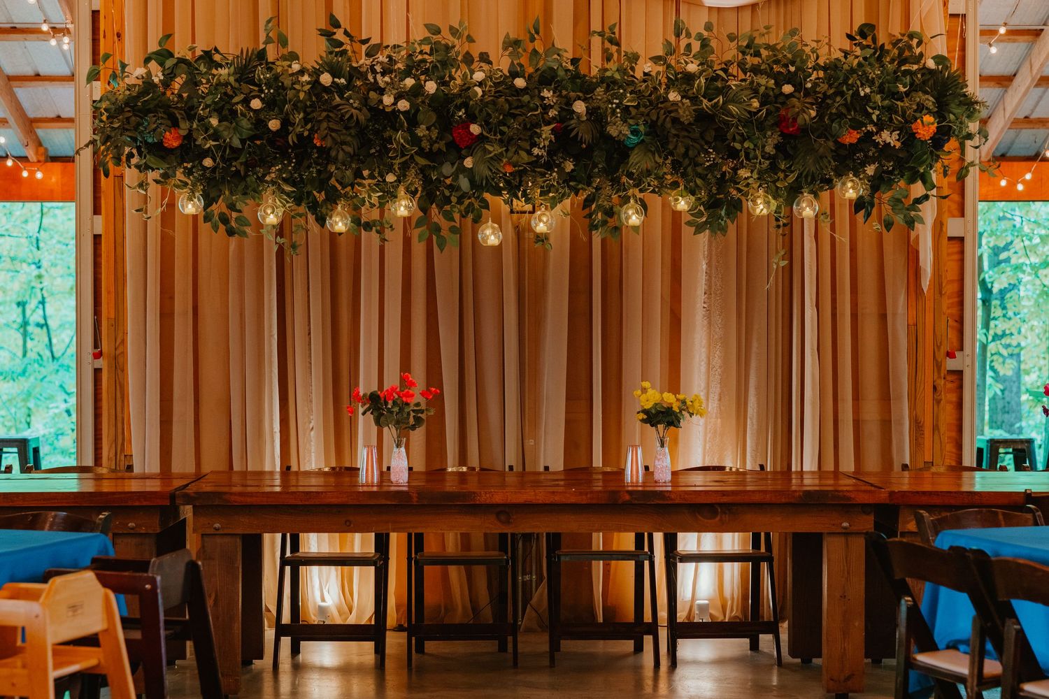 Rustic barn reception head table with lush floral ceiling installation and string lights. Documentary style wedding photos.