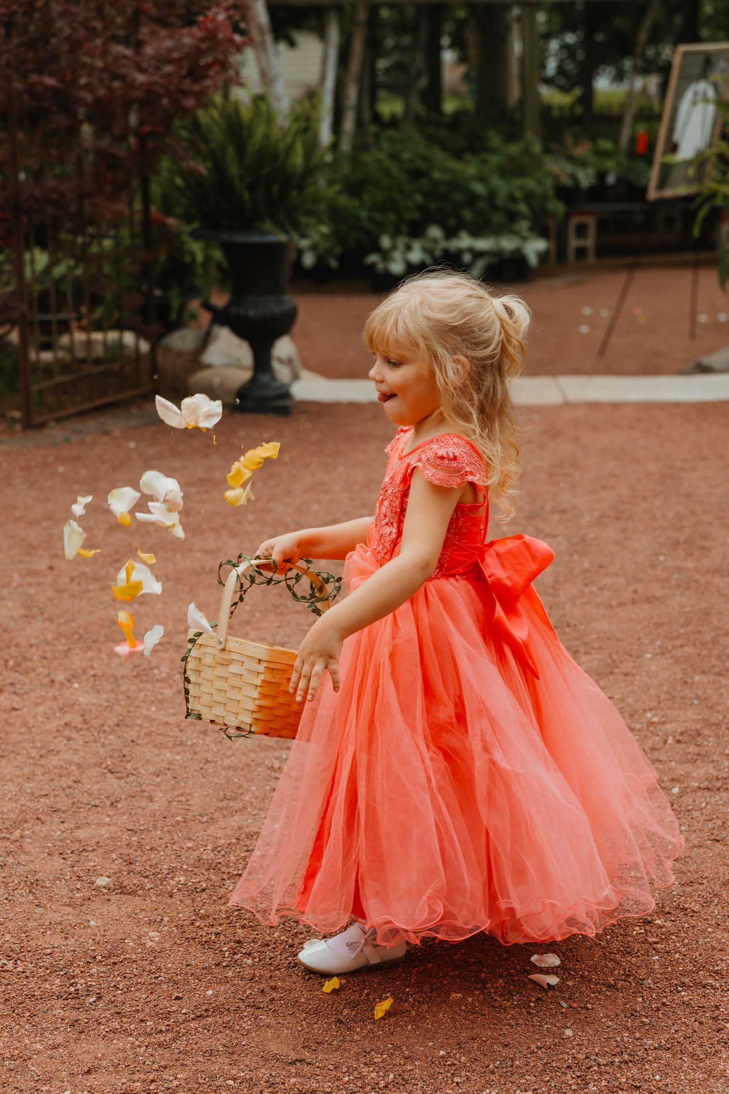 Young flower girl in coral tulle dress tossing petals from wicker basket outdoors at wedding. Chicagoland wedding venues.