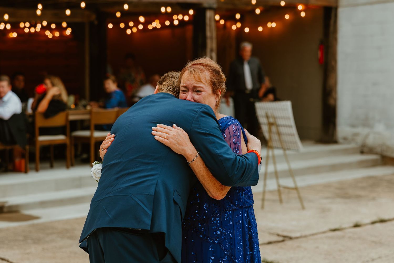 Emotional mother and son share heartfelt hug during wedding reception at outdoor barn venue. Northwest Indiana wedding venues.