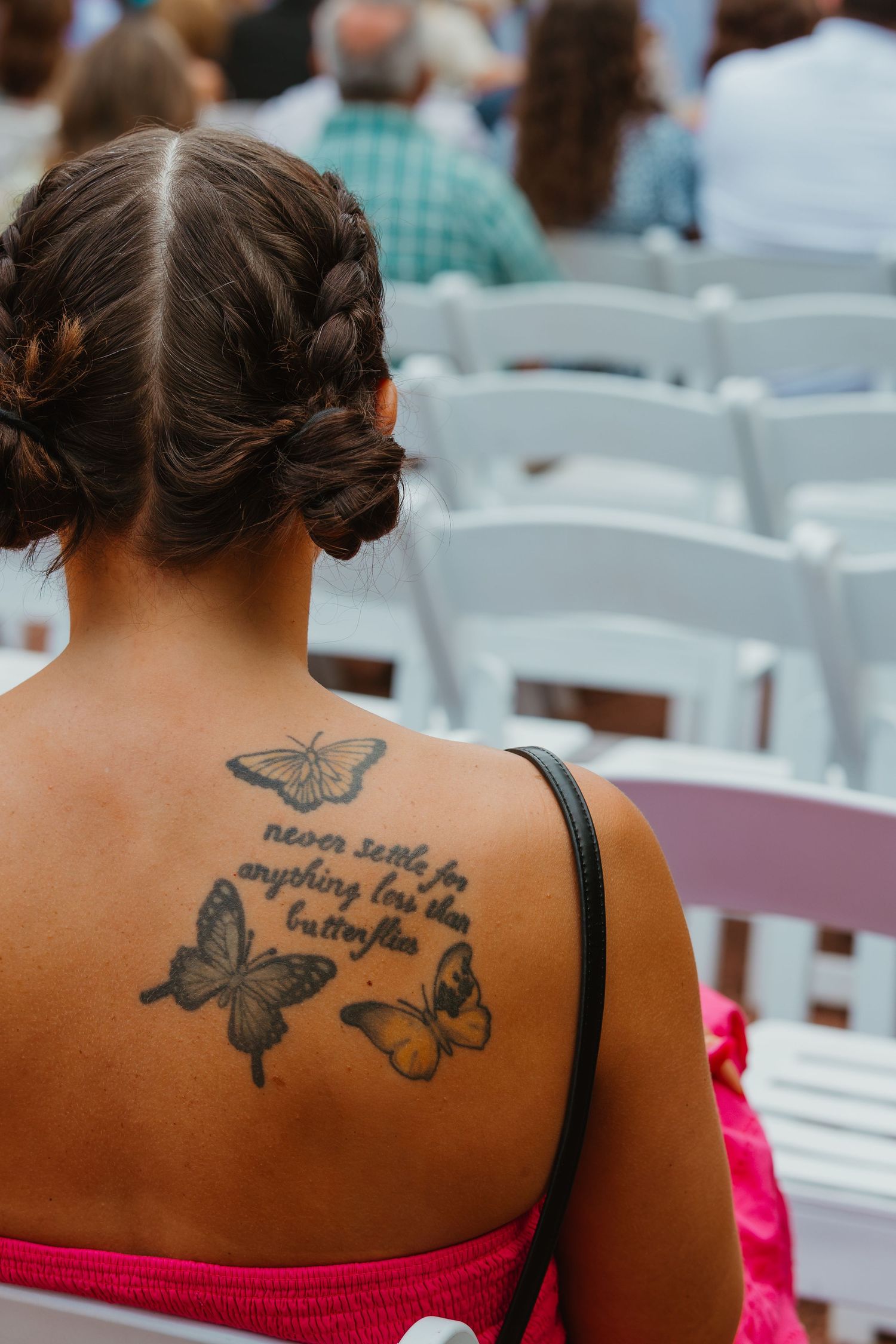 Wedding guest with butterfly tattoo and braided updo seated at outdoor ceremony in pink dress. Chicagoland wedding venues.