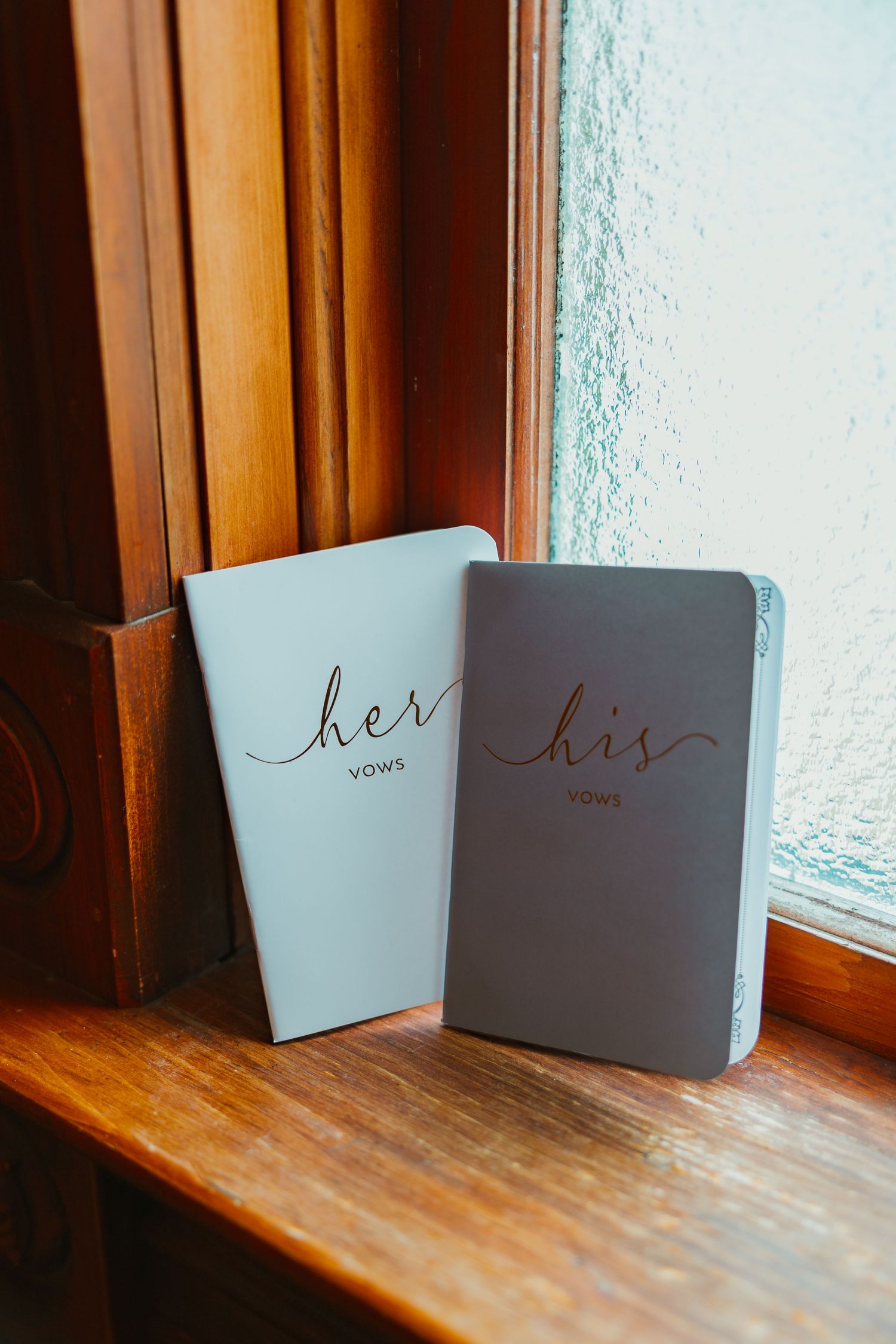 His and her vows booklets leaning against a window on a wooden ledge. Michigan elopement.