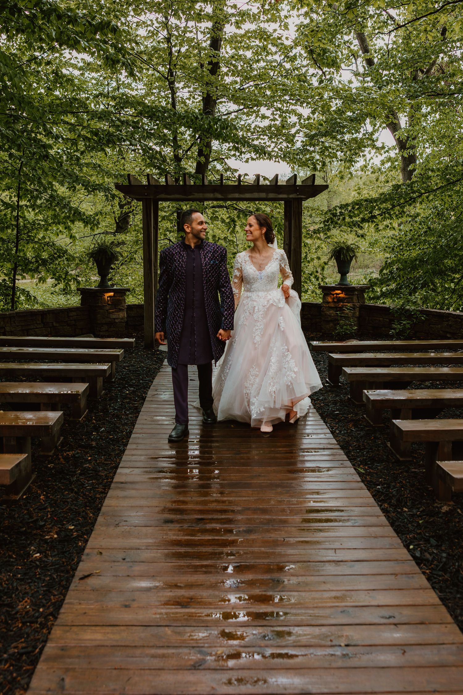 Bride and groom walking hand in hand down a wet wooden aisle in an outdoor forest ceremony. Documentary style wedding photos.