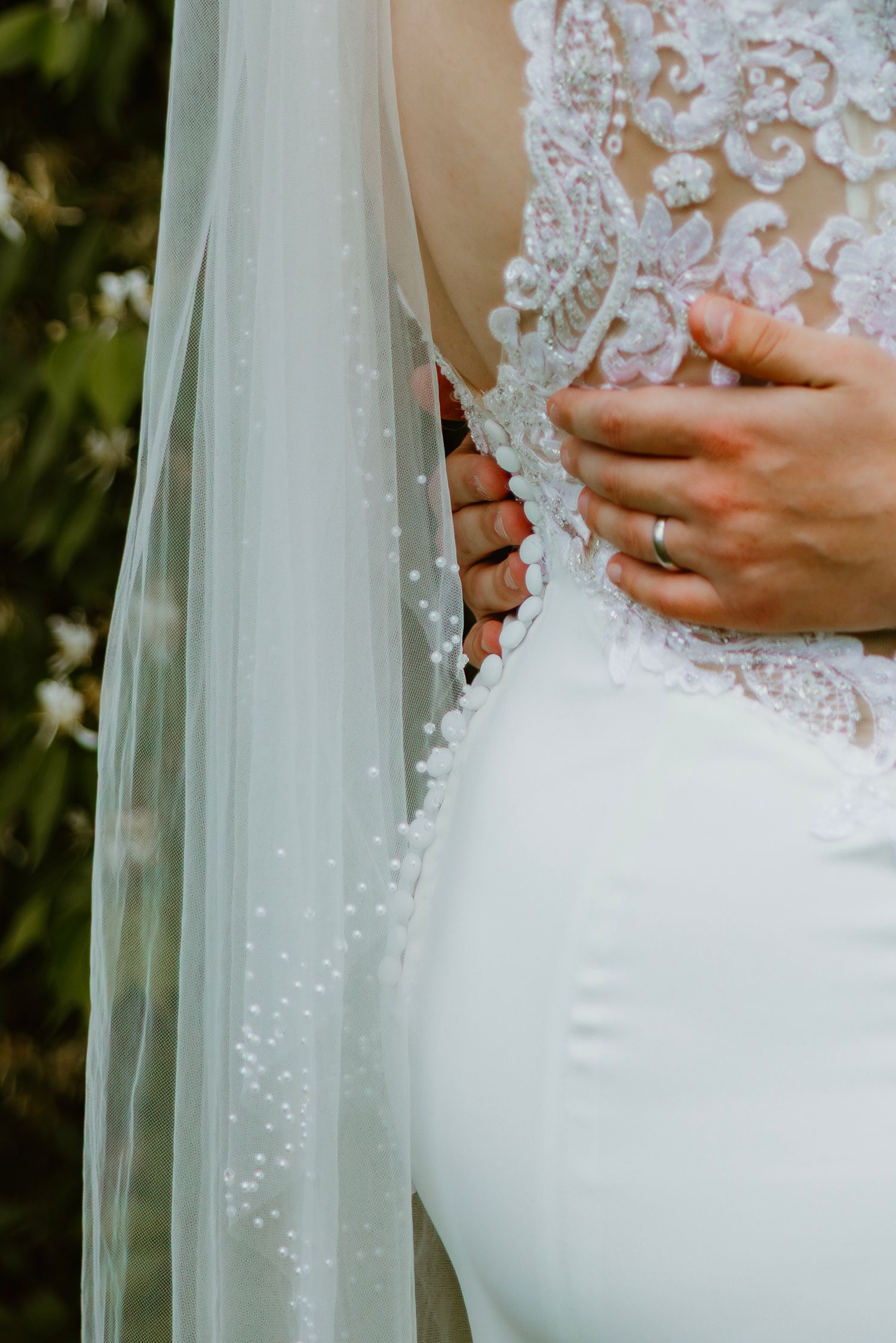 Close-up of bride in pearl-adorned lace wedding gown with flowing veil held by groom. Northwest Indiana event center wedding photos.