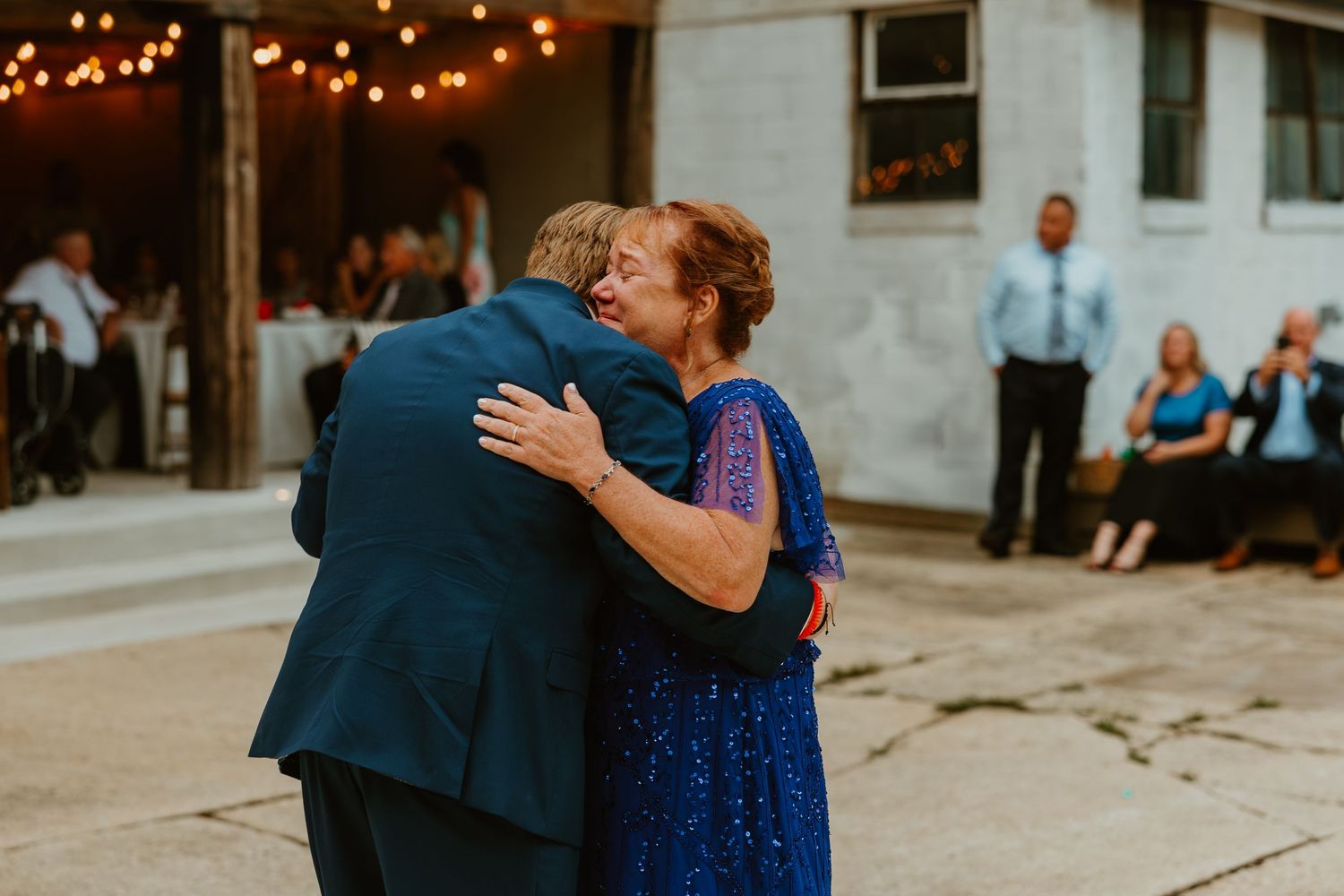 Groom sharing a warm embrace with older woman in blue sequin dress at outdoor wedding reception. Northwest Indiana wedding venues.
