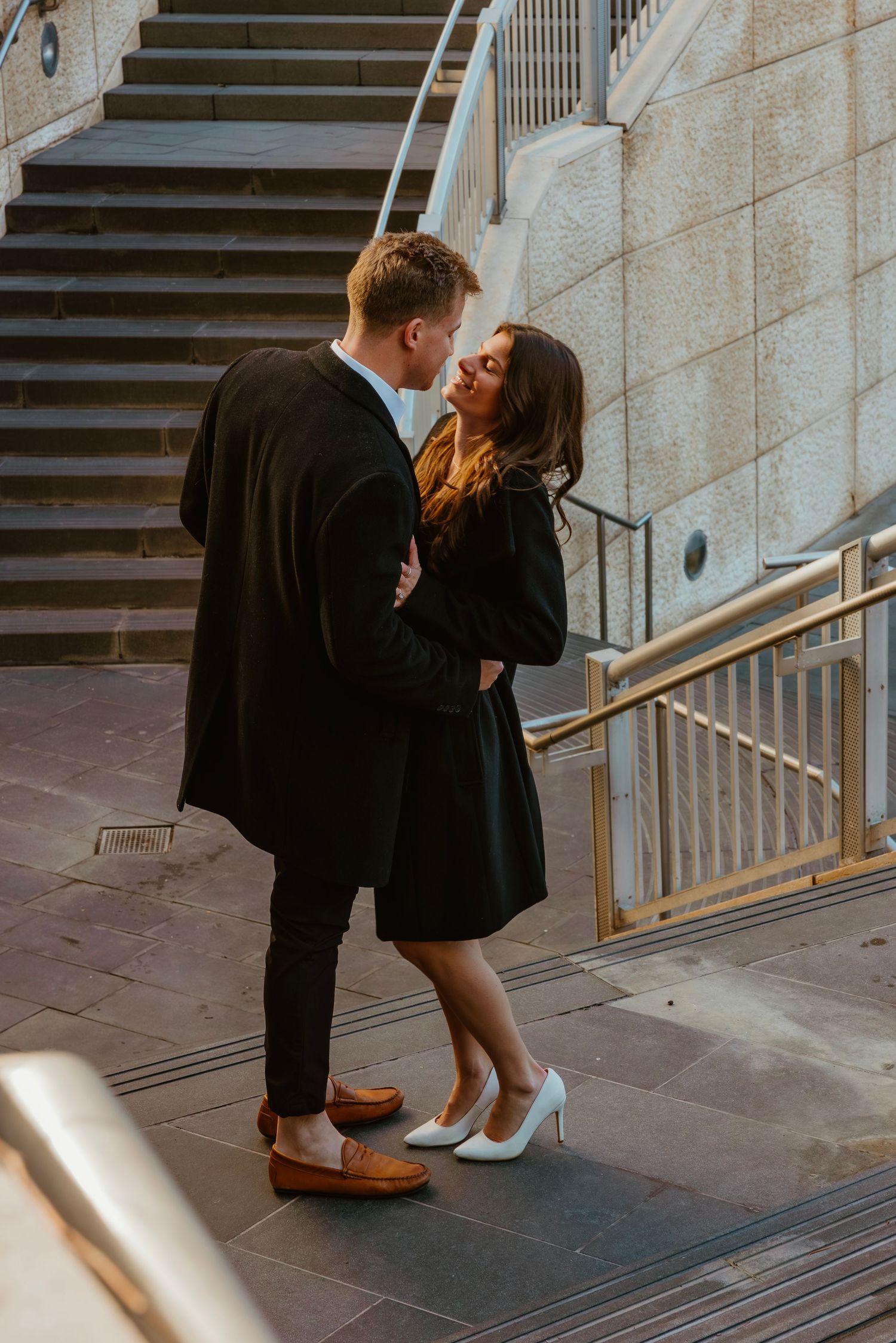 Couple leaning in for a kiss near a staircase railing in an urban outdoor setting. Outdoor Chicago engagement photos.