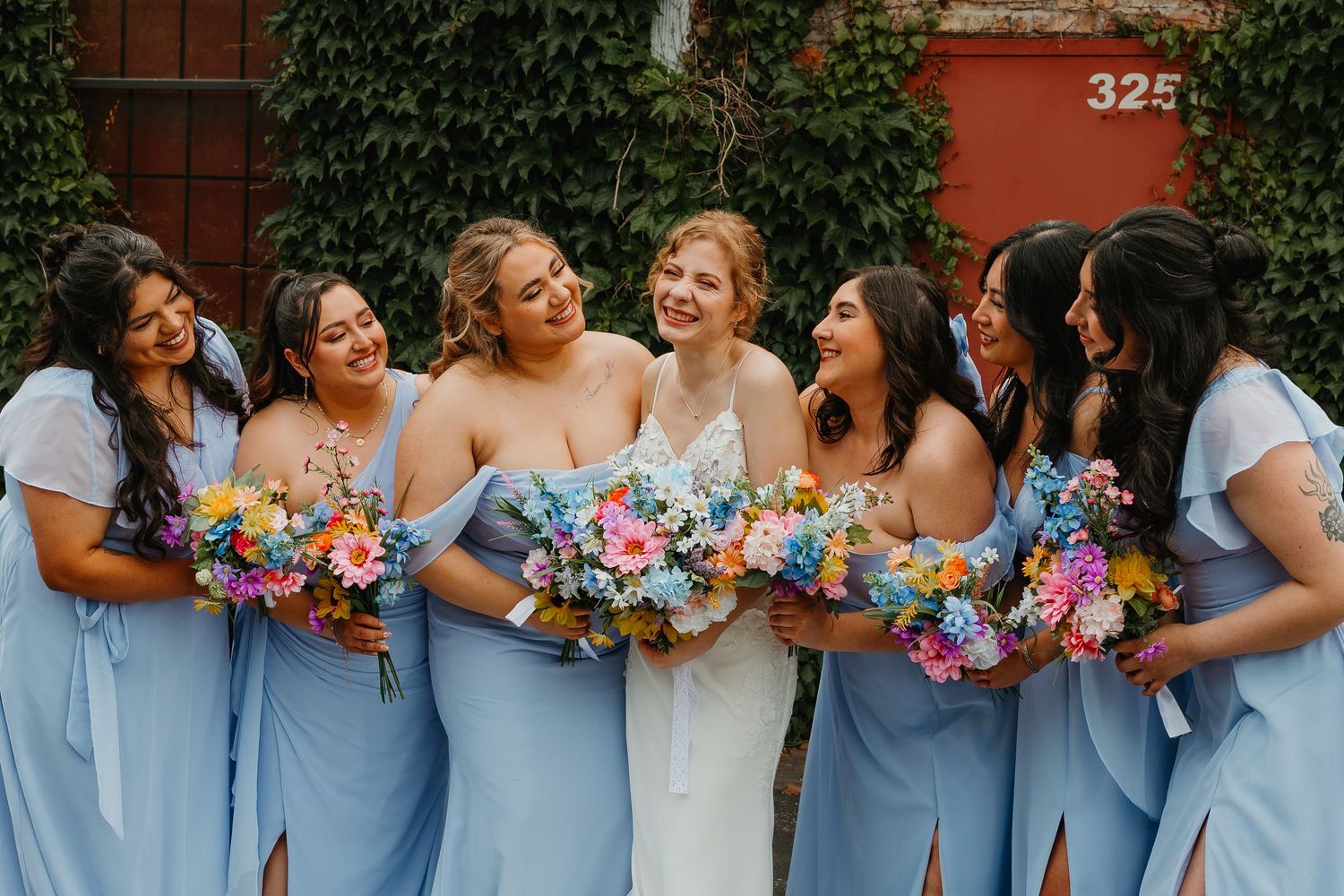 Bride and bridesmaids in light blue gowns laughing together holding vibrant floral bouquets. Chicagoland wedding venues.