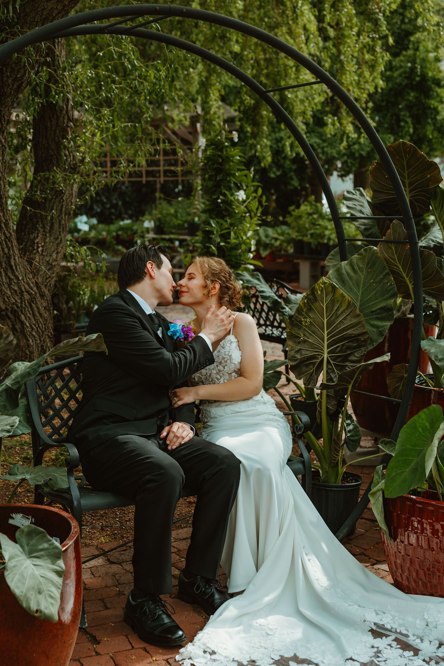 Bride and groom kiss under metal arch surrounded by tropical plants in garden. Chicagoland wedding venues.