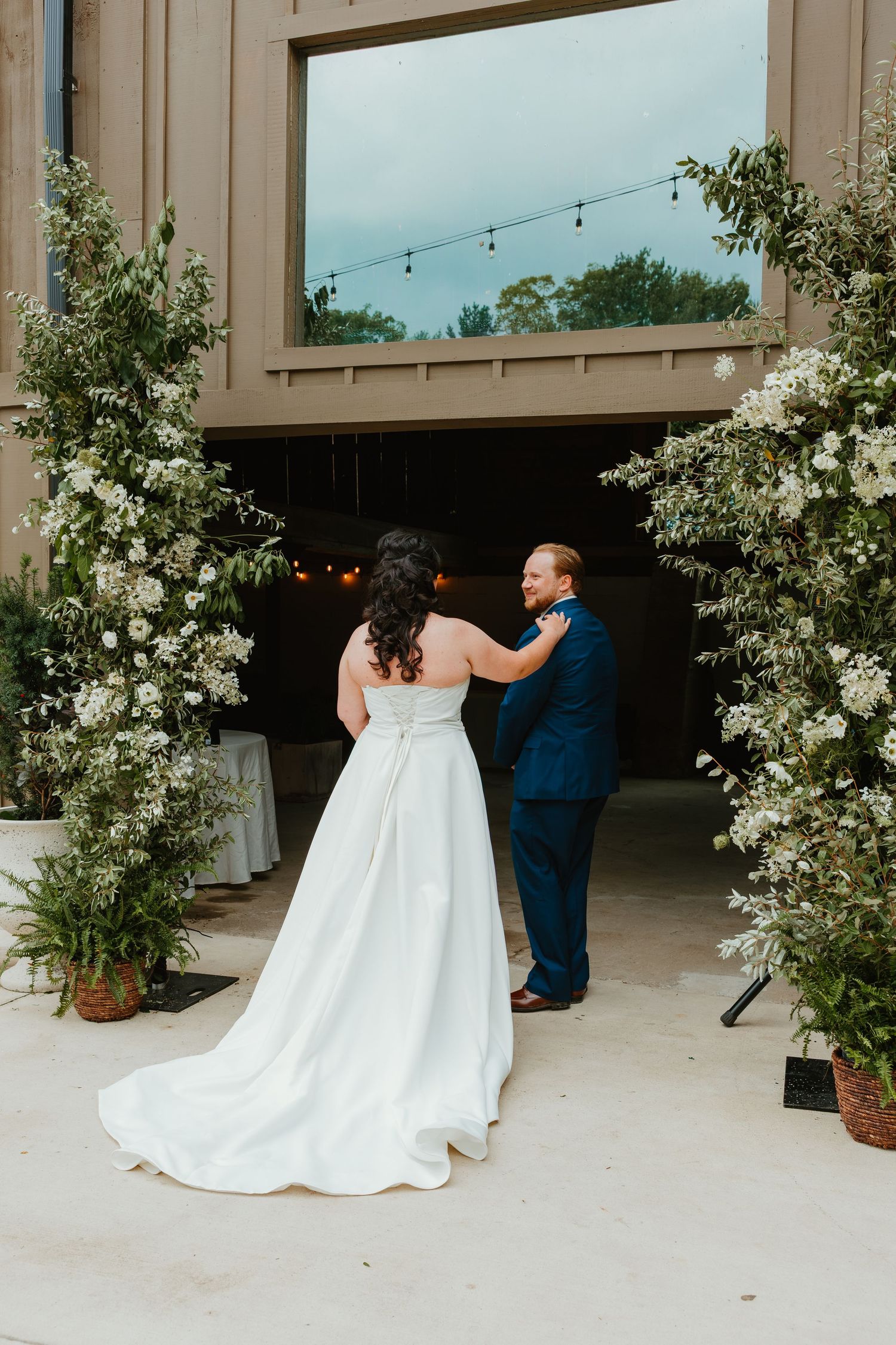 Bride and groom share a tender first look moment framed by lush white floral arrangements at a barn wedding venue. Northwest Indiana wedding