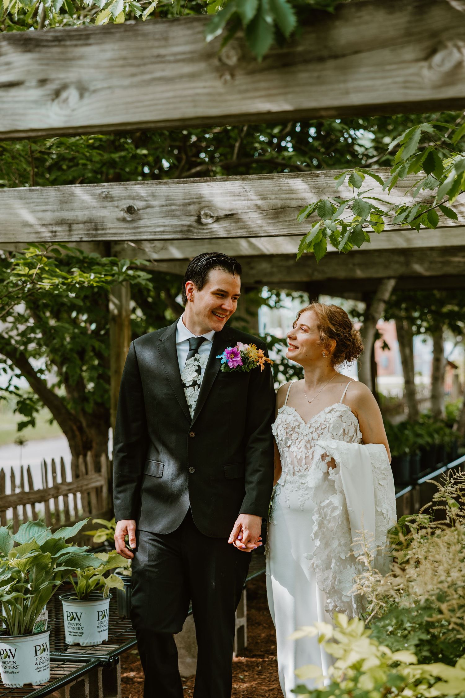 Bride and groom walk hand in hand under wooden pergola surrounded by greenery. Chicagoland wedding venues.