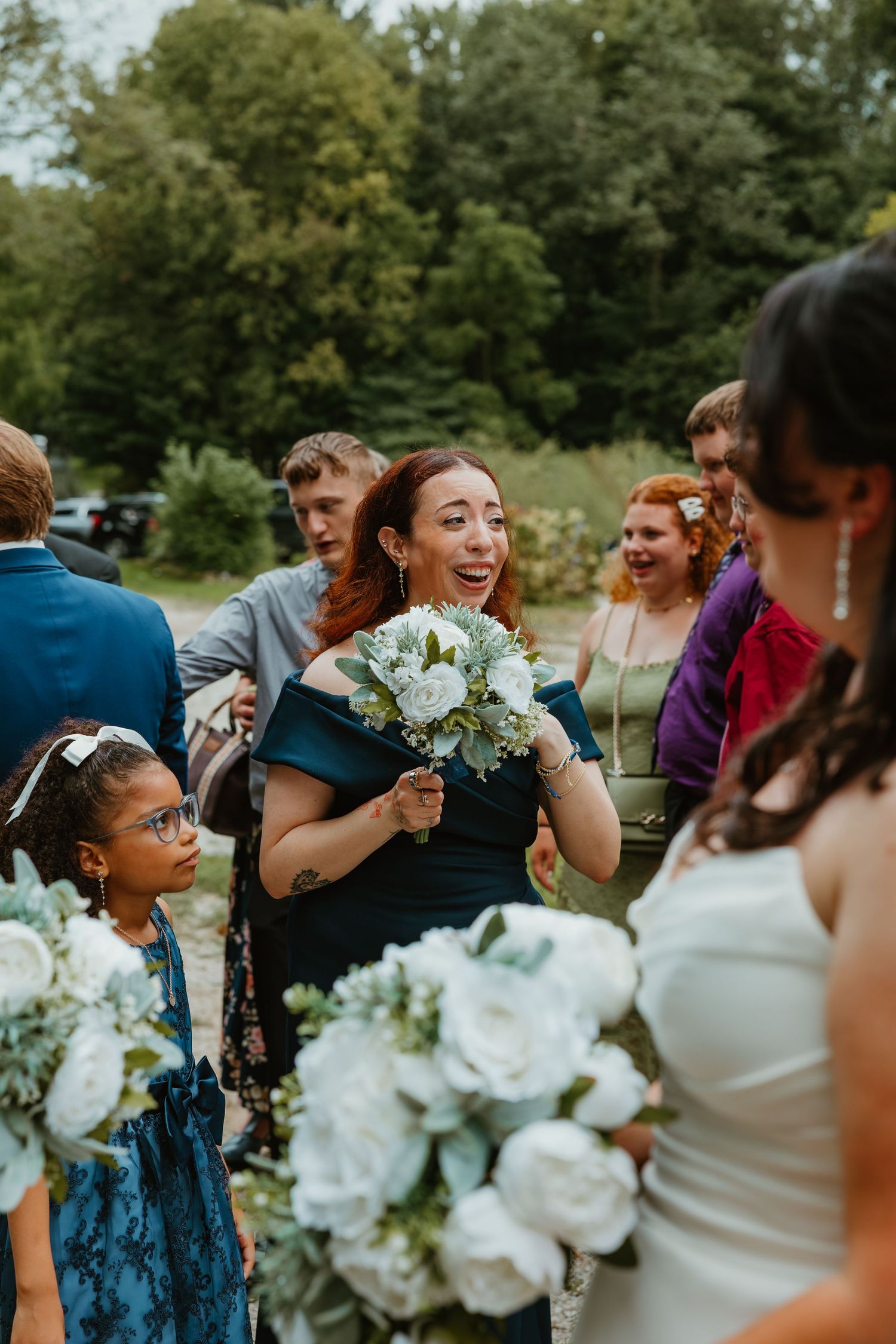 Emotional bridesmaid in teal holds white bouquet while greeting the bride outdoors after a wedding ceremony. Northwest Indiana wedding venue